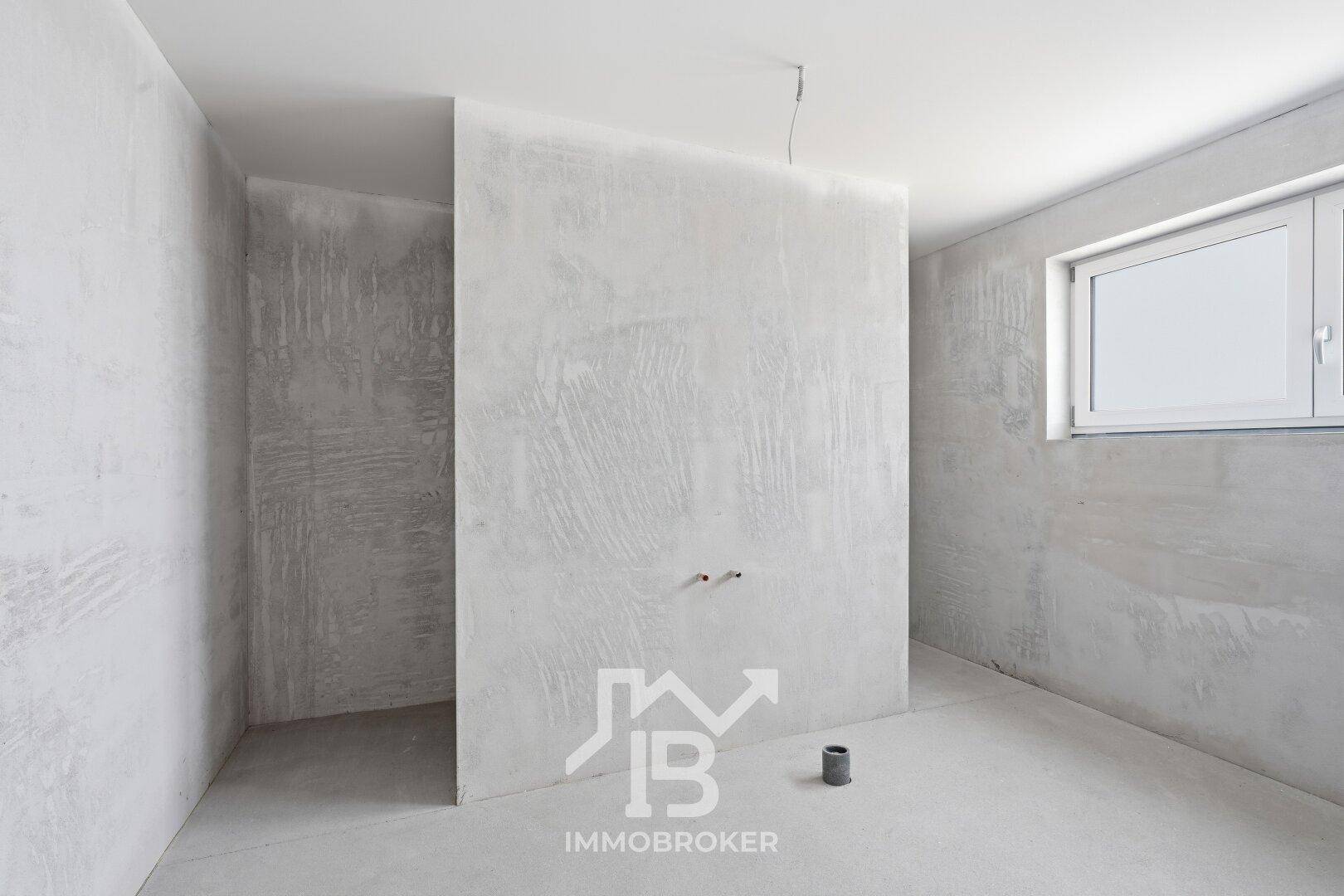 Unfertiges Badezimmer im Rohbauzustand mit Betonwänden und Fenster.