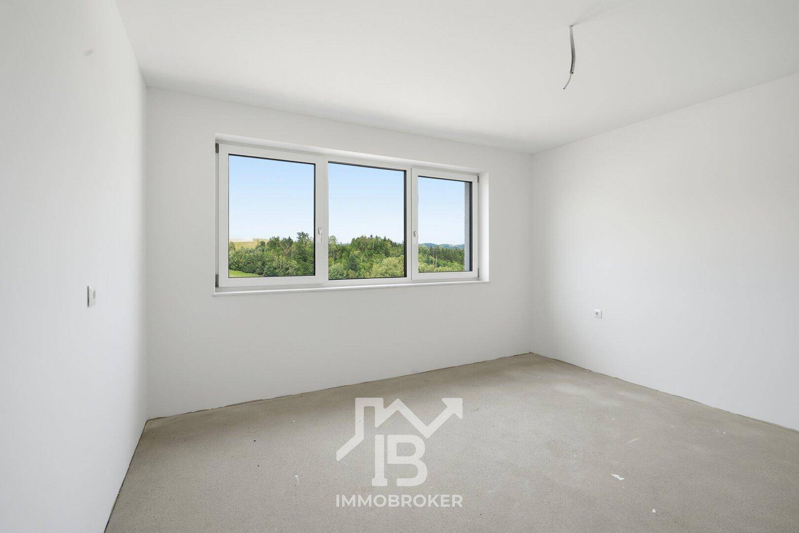 Heller Raum im Rohbau mit Betonboden und großem Fenster mit Blick auf die Landschaft.