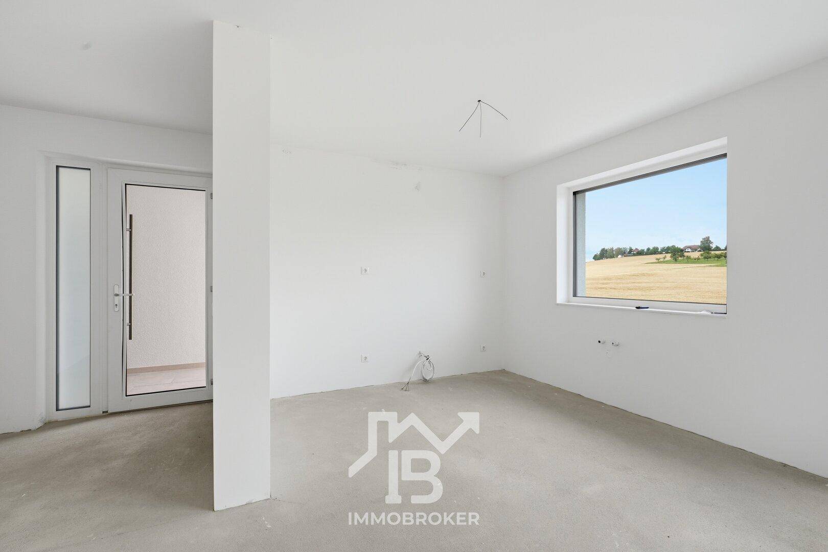 Unfertiger Raum mit Betonboden, einer Säule und einer Glastür zum Außenbereich.
