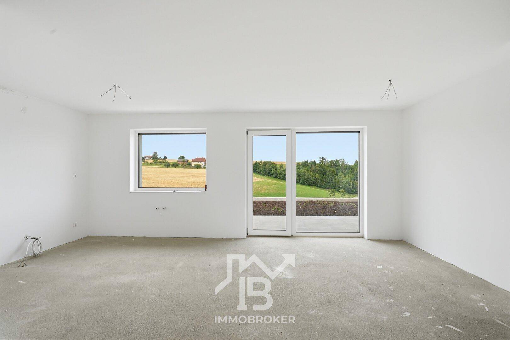 Heller Raum im Rohbauzustand mit Betonboden, Fenster und Glastür zum Außenbereich.