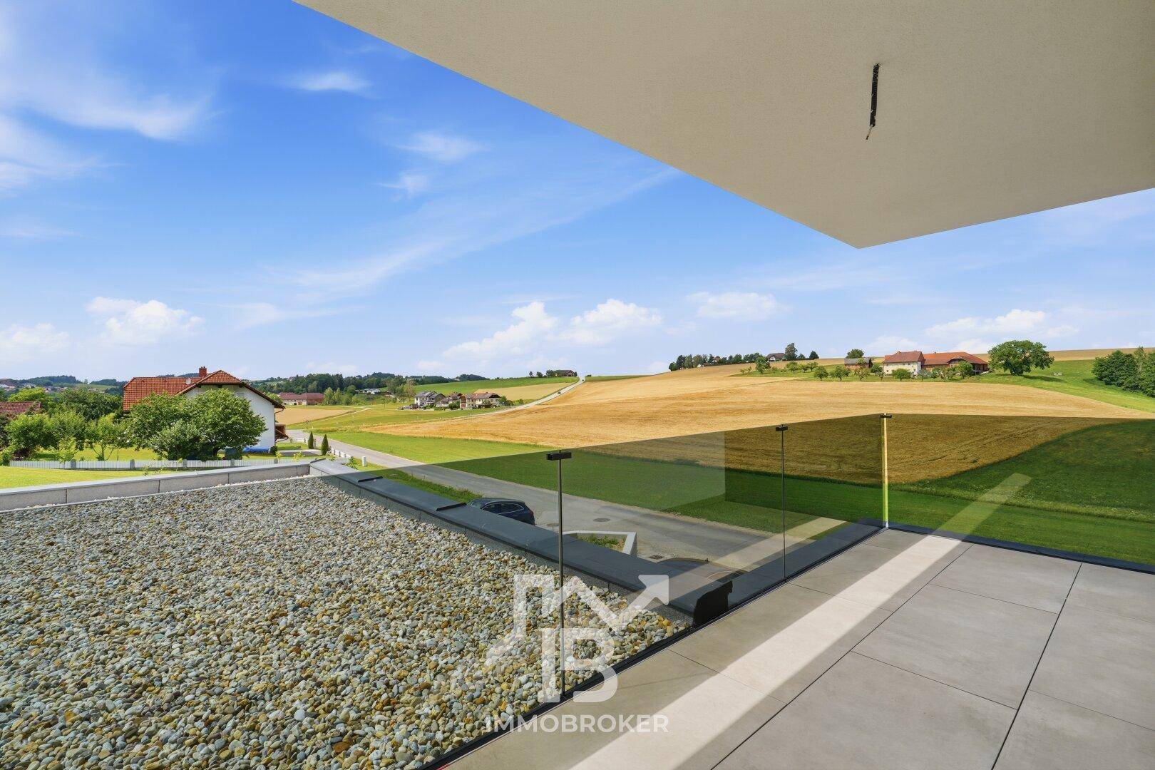 Dachterrasse mit Kiesbelag, Glasgeländer und weitem Blick über die ländliche Umgebung.