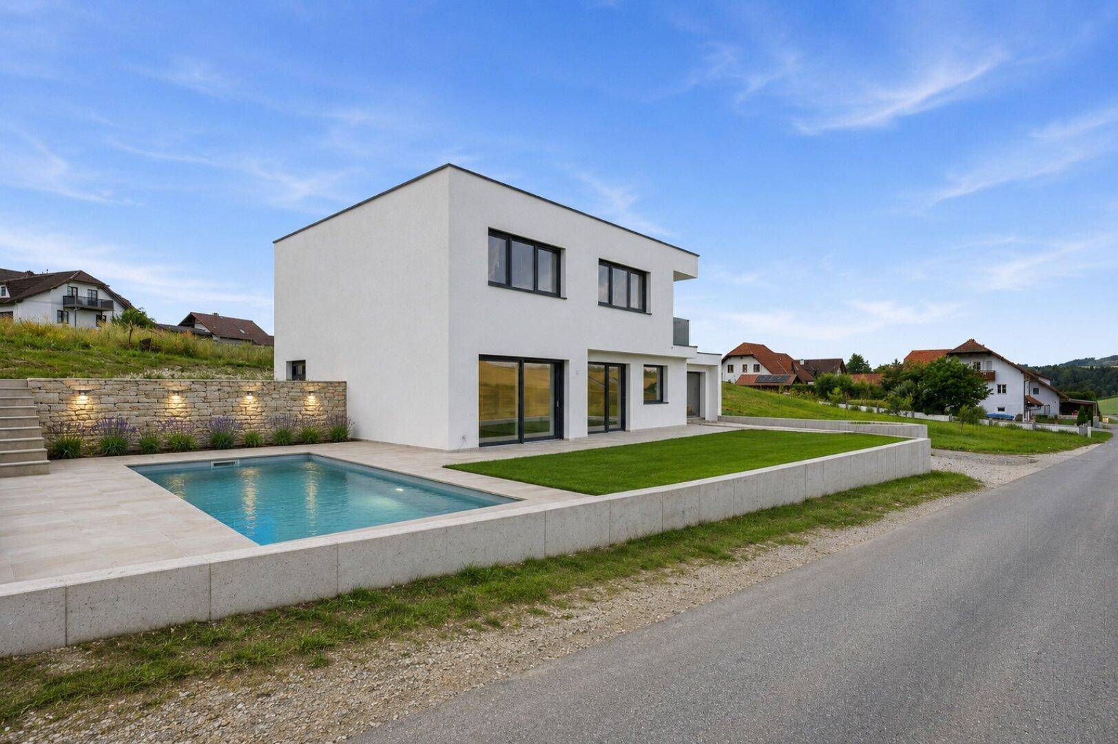 Modernes Einfamilienhaus mit Swimmingpool, gepflegtem Rasen und einer Steinmauer im Außenbereich.