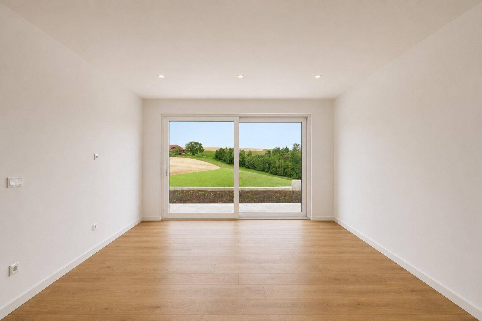 Geräumiger Wohnraum mit Holzfußboden und großen Fenstern, die einen weiten Blick ins Grüne bieten.