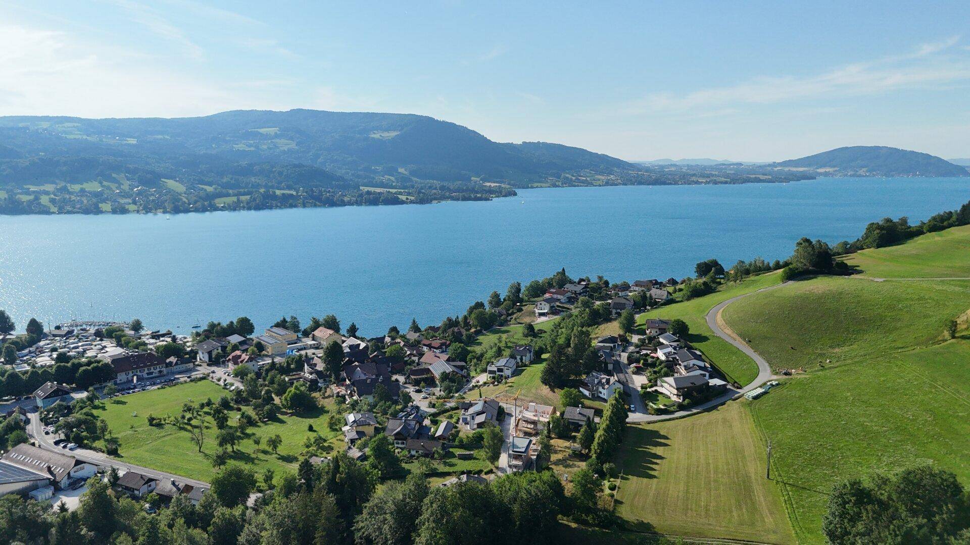 Weitläufige Luftaufnahme einer malerischen Seenlandschaft mit umliegenden Hügeln und Dörfern.