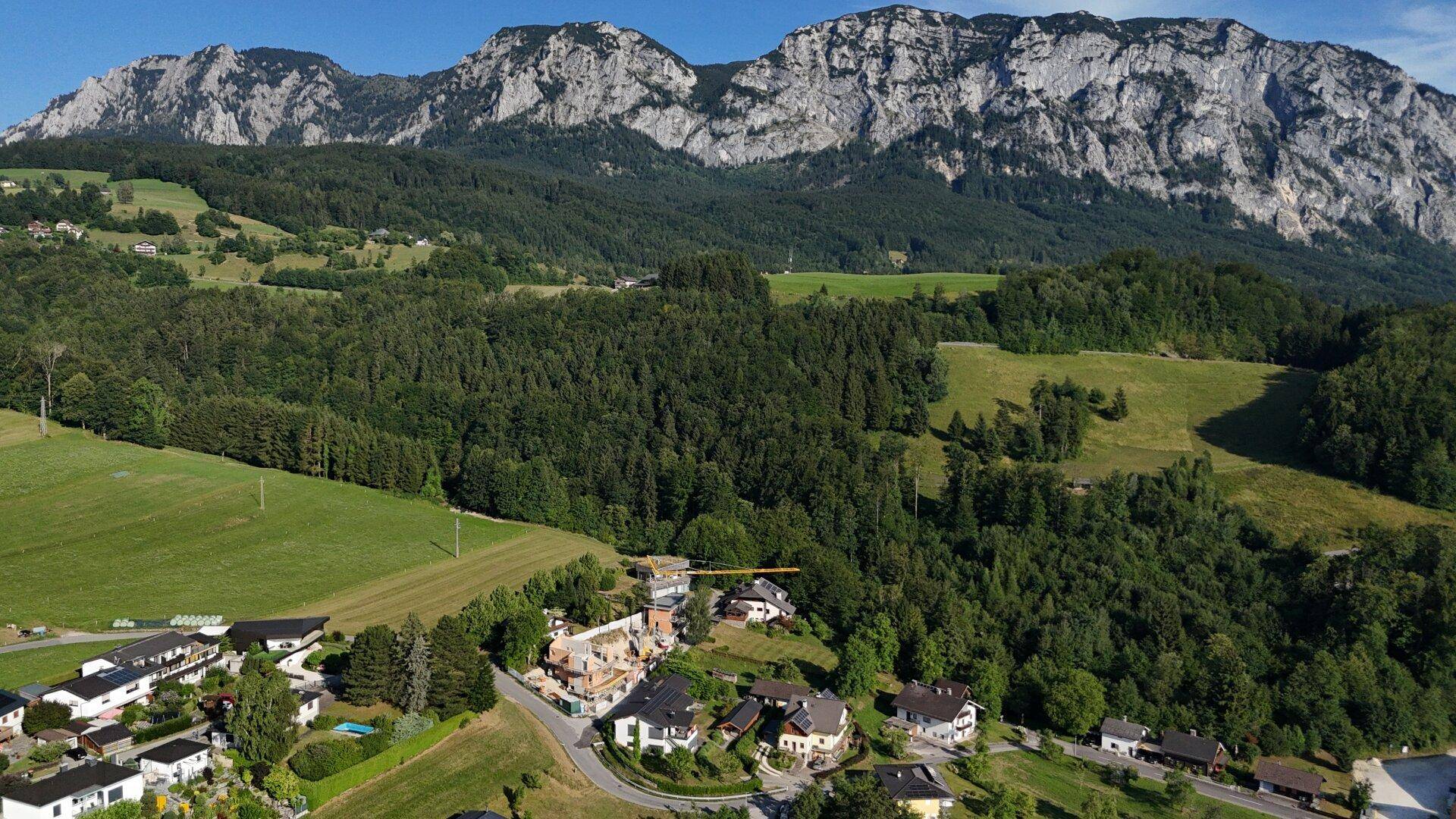 Panoramablick auf eine beeindruckende Berglandschaft mit bewaldeten Hängen und kleinen Siedlungen.