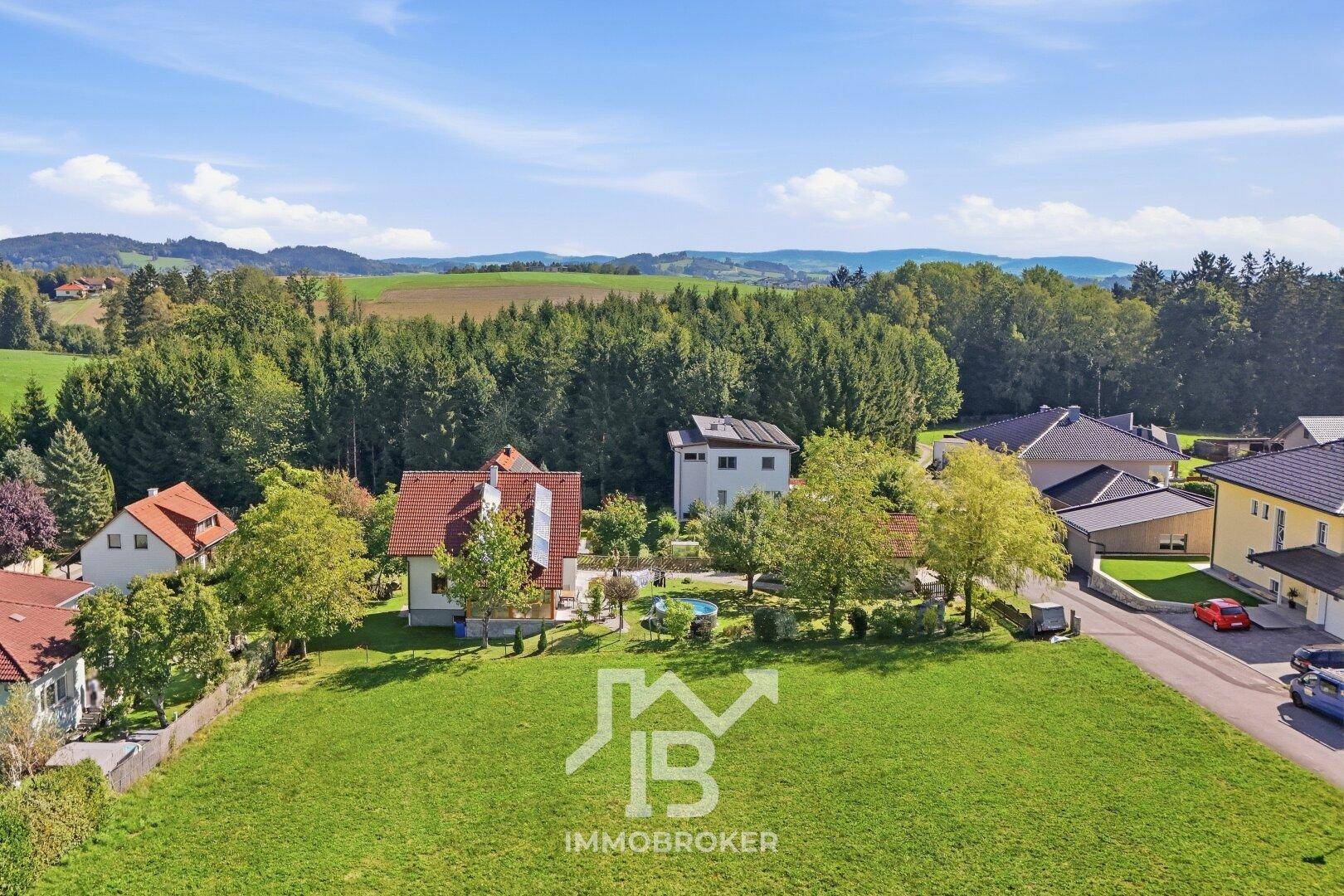 Luftaufnahme eines großen grünen Grundstücks mit Blick auf die umliegende Wohnbebauung und Wälder.