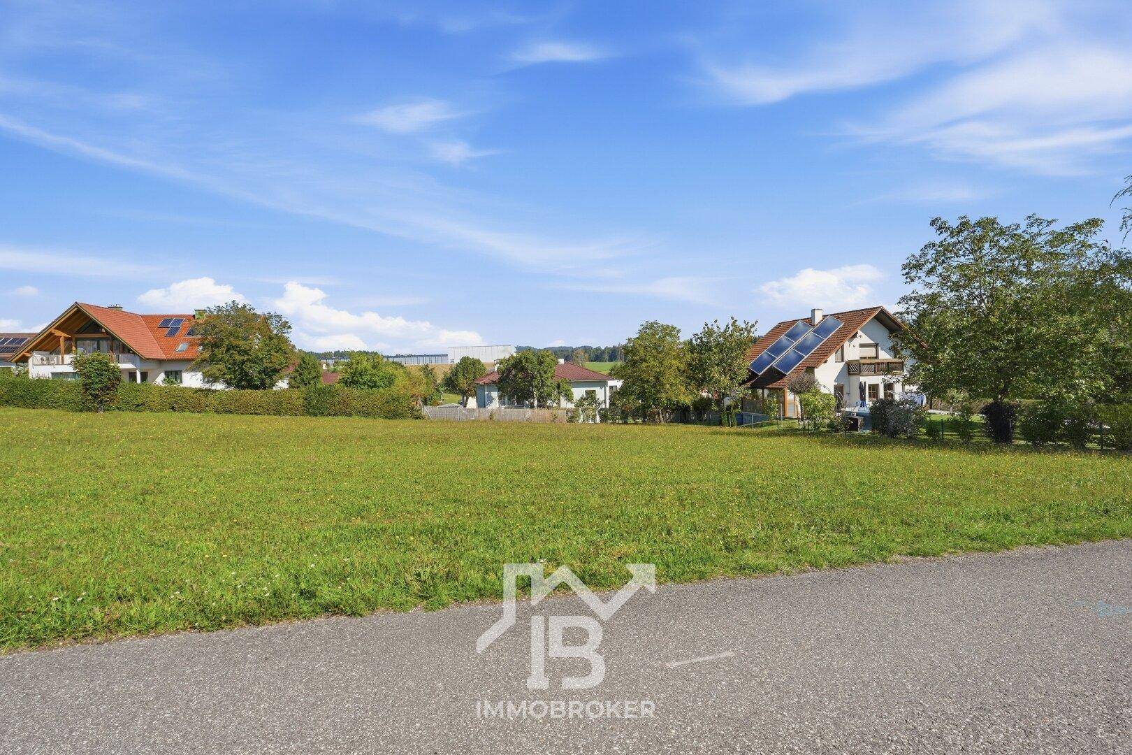 Blick vom Grundstück über die grüne Wiese zu den Nachbarhäusern und dem bewaldeten Horizont.