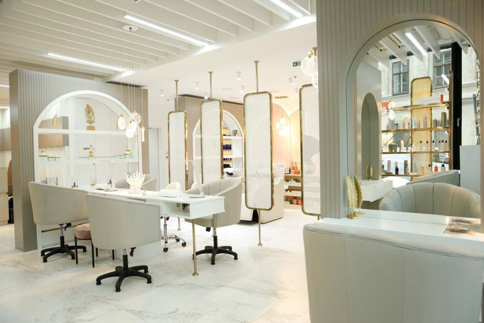 Heller Behandlungsbereich mit mehreren Maniküre-Stationen, eleganten Stühlen und dekorativen Raumteilern.