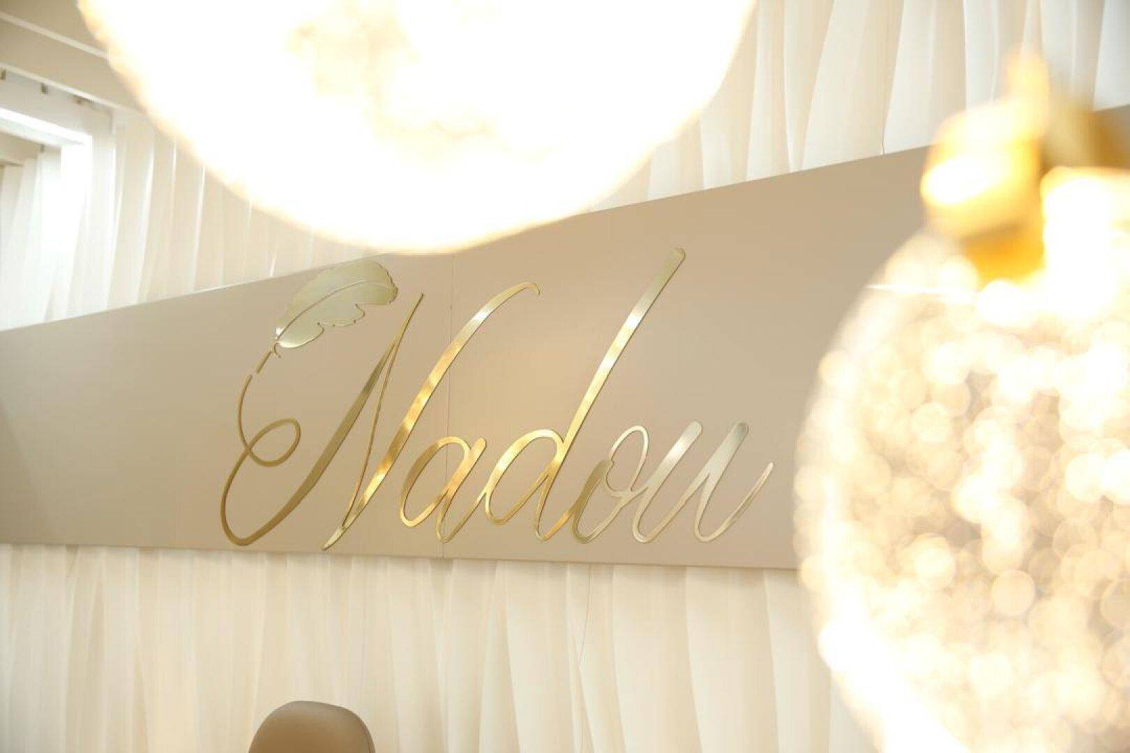 Goldene Schriftzüge auf einer hellen Wand, umgeben von weichen, transparenten Vorhängen und warmen Lichtquellen.