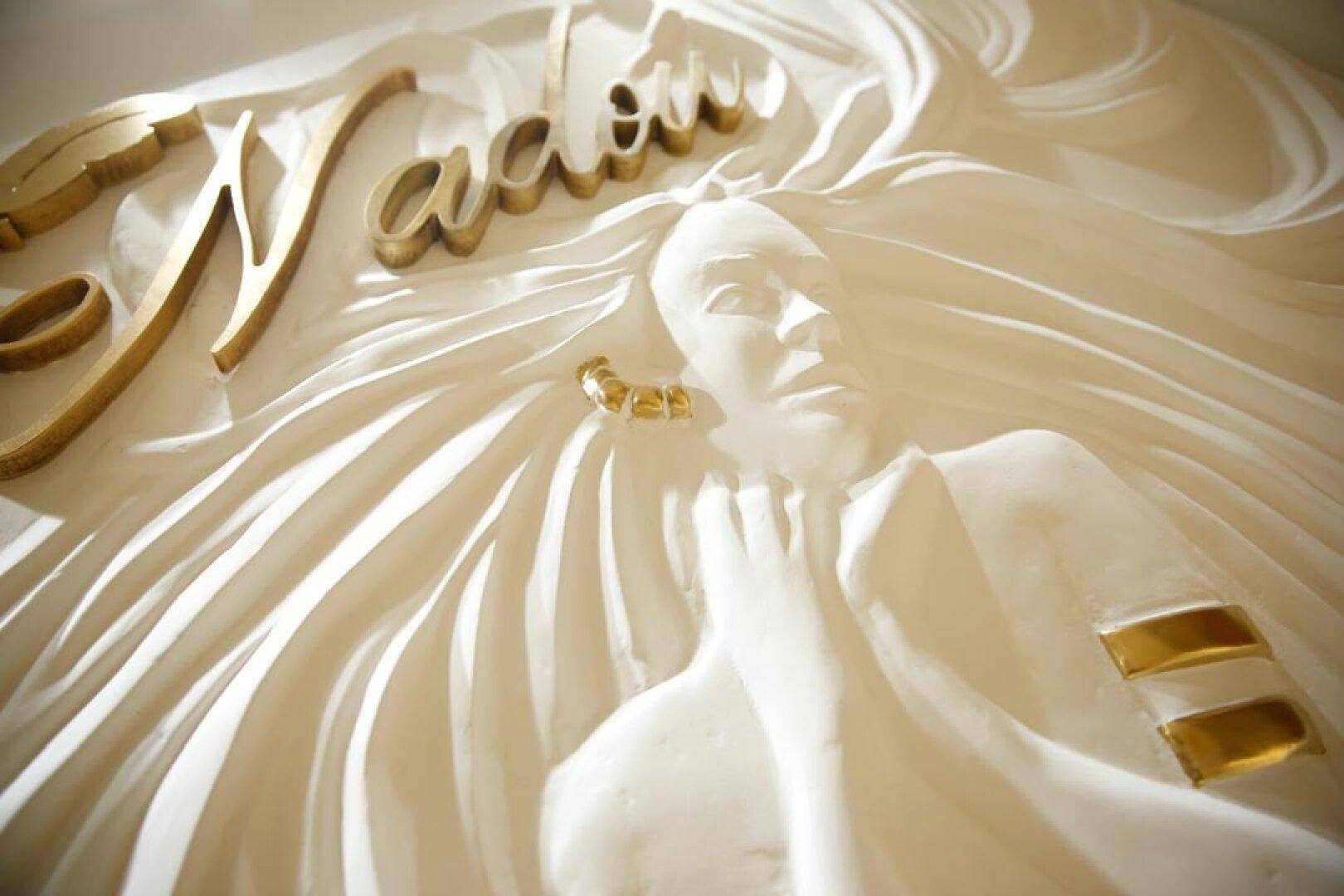 Nahaufnahme einer kunstvollen Wanddekoration mit goldenen Schriftzügen und einer reliefartigen Frauenfigur.