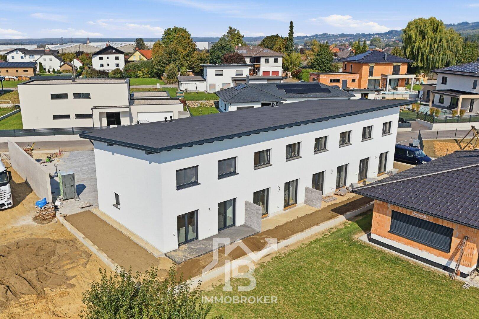 Rückansicht der modernen Reihenhäuser mit Terrassen und Gärten in ländlicher Umgebung.