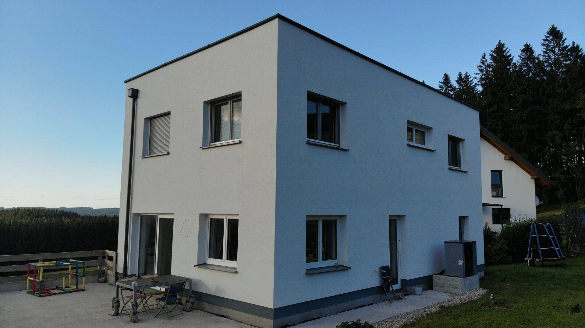 Ansicht eines modernen Einfamilienhauses mit weißer Fassade und kleiner Terrasse im Grünen.
