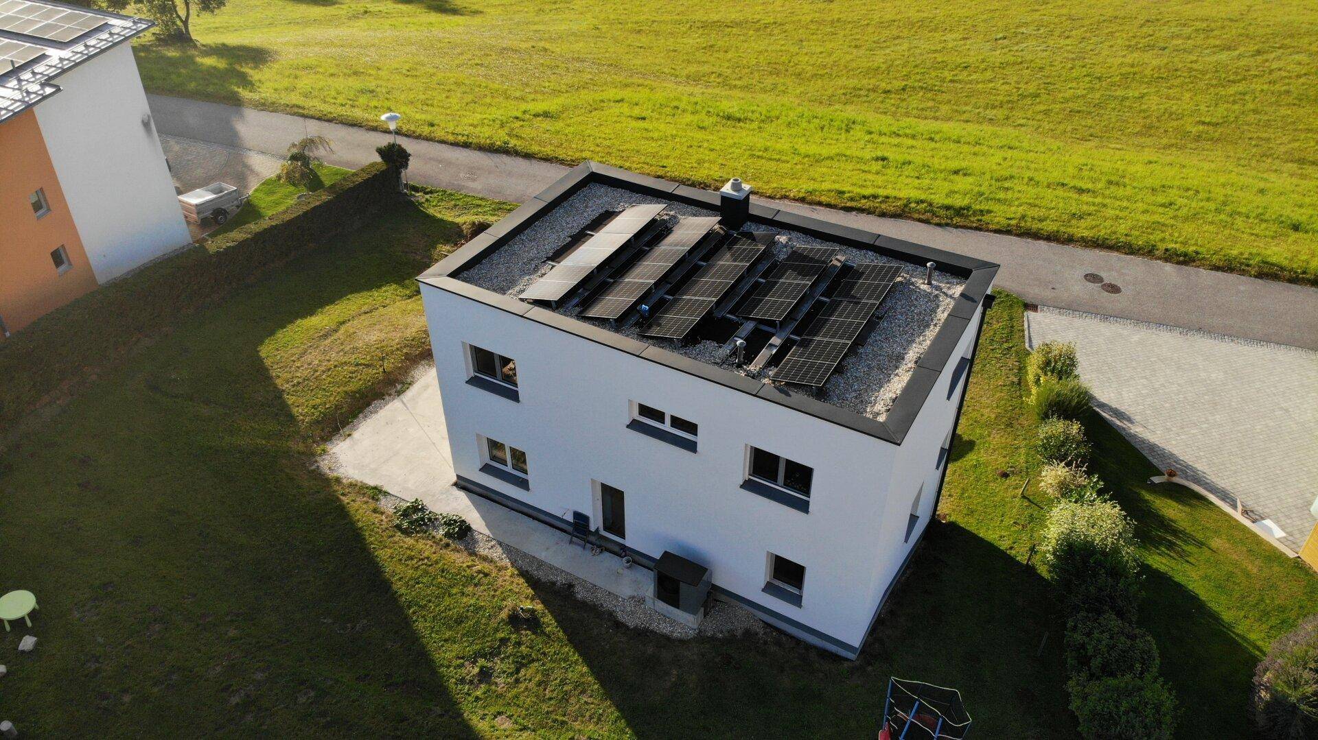 Luftaufnahme eines modernen Hauses mit Flachdach und Photovoltaikanlage in ländlicher Umgebung.