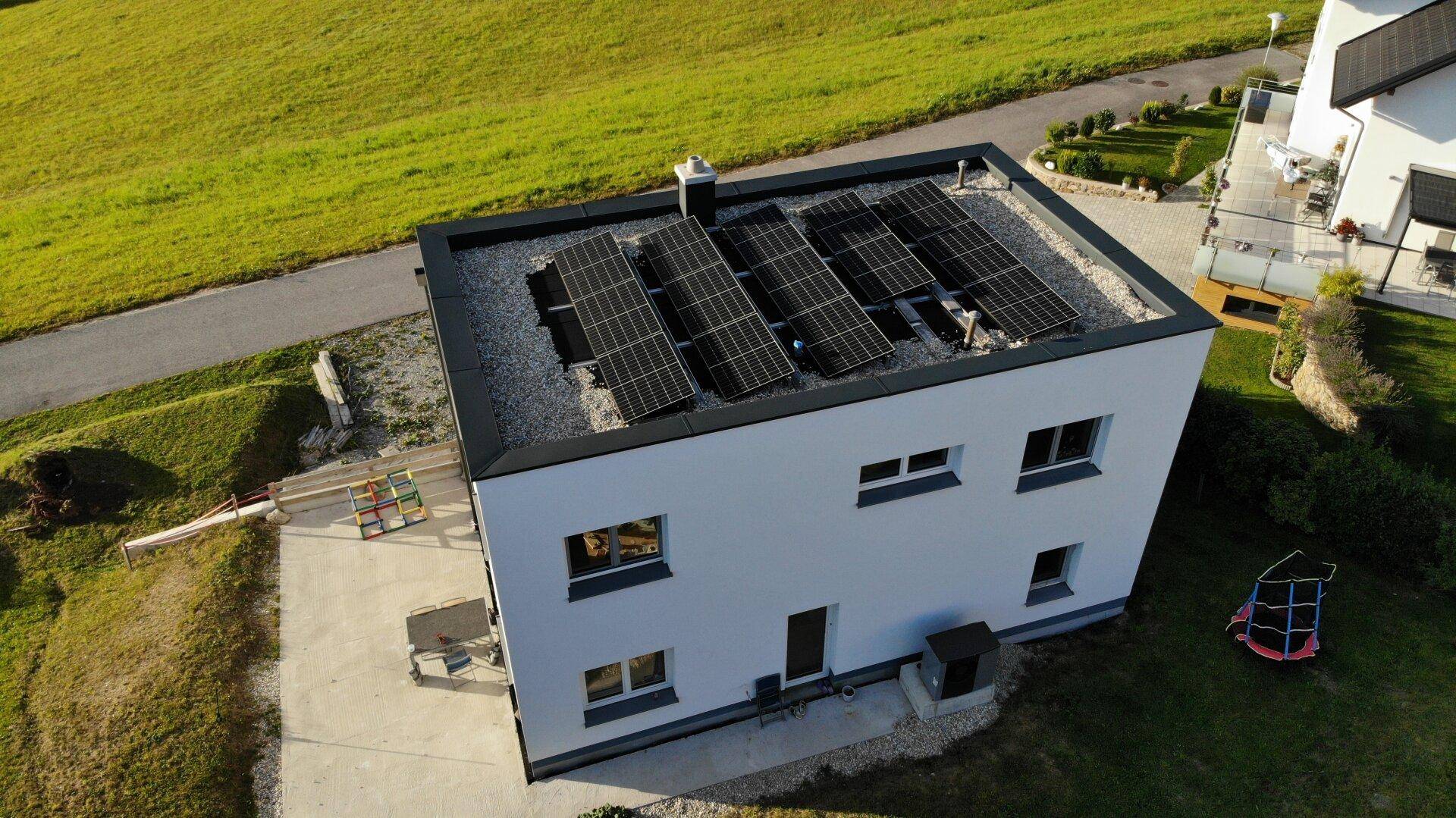 Vogelperspektive des Hauses mit Solarmodulen auf dem Flachdach und weitläufiger Grünfläche.