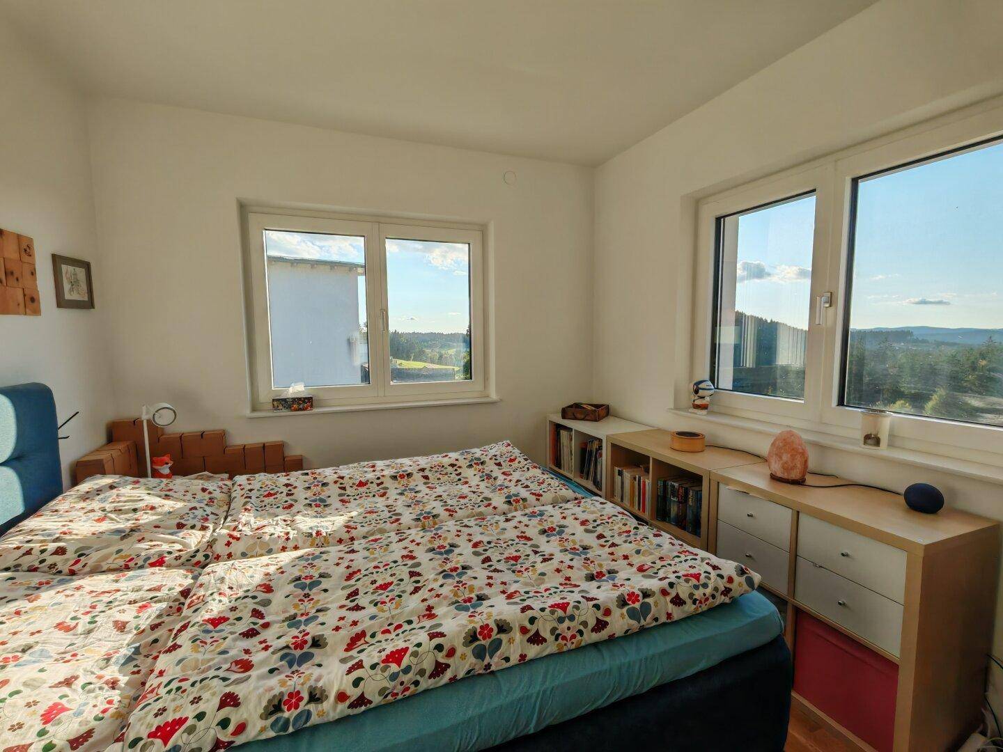 Helles Schlafzimmer mit Doppelbett, Holzboden und Fenstern mit Blick in die Natur.
