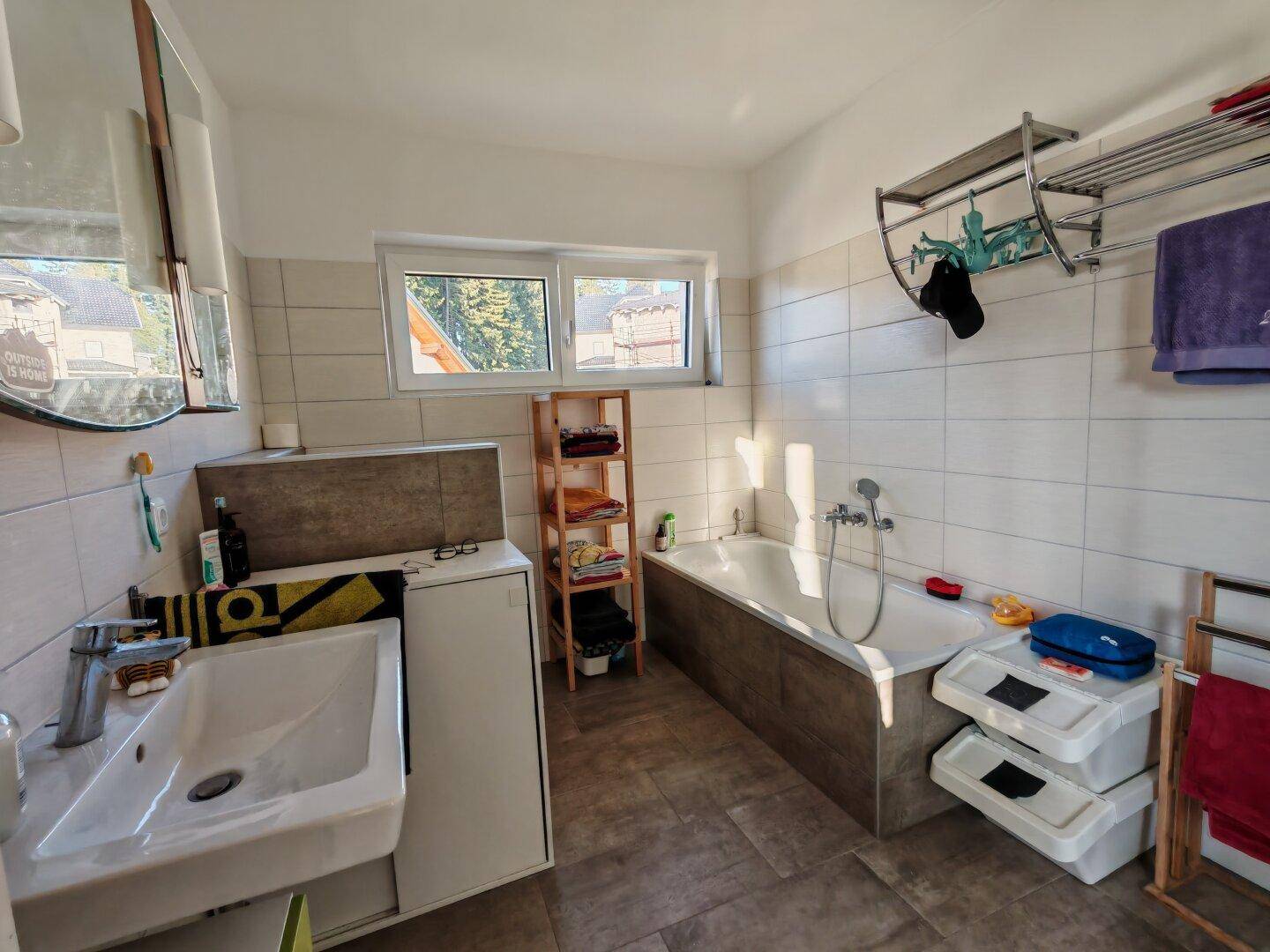 Badezimmer mit Badewanne, Waschbecken und hellen Fliesen, ausgestattet mit einem Fenster.