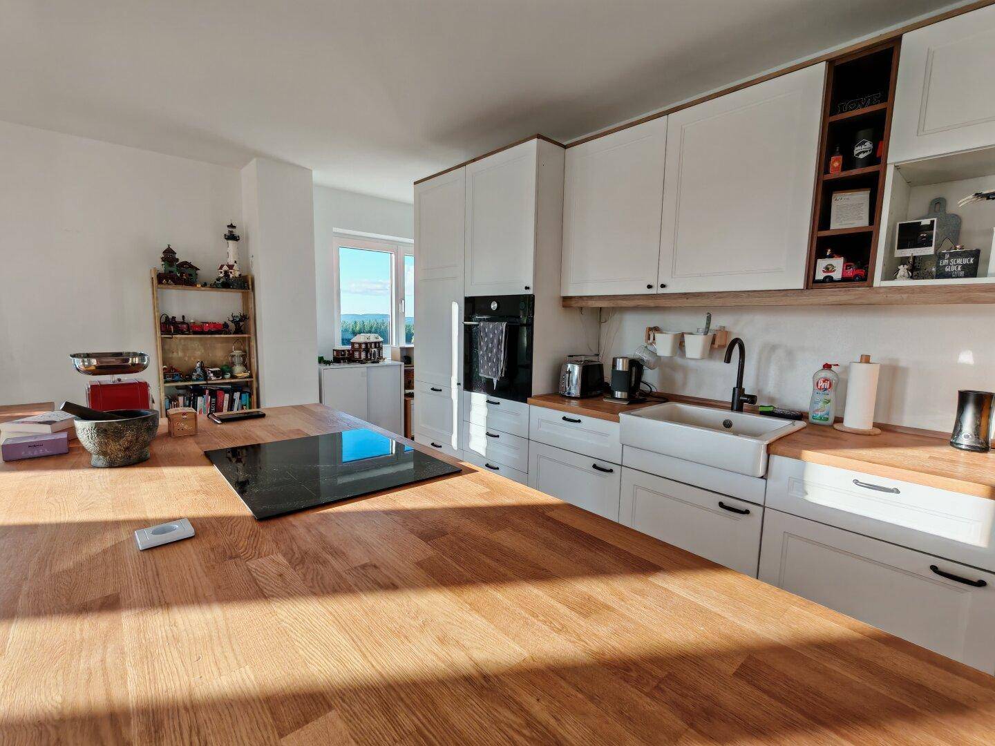 Moderne Küche mit weißen Schränken, Holztheke und integrierten Geräten in sonnigem Ambiente.