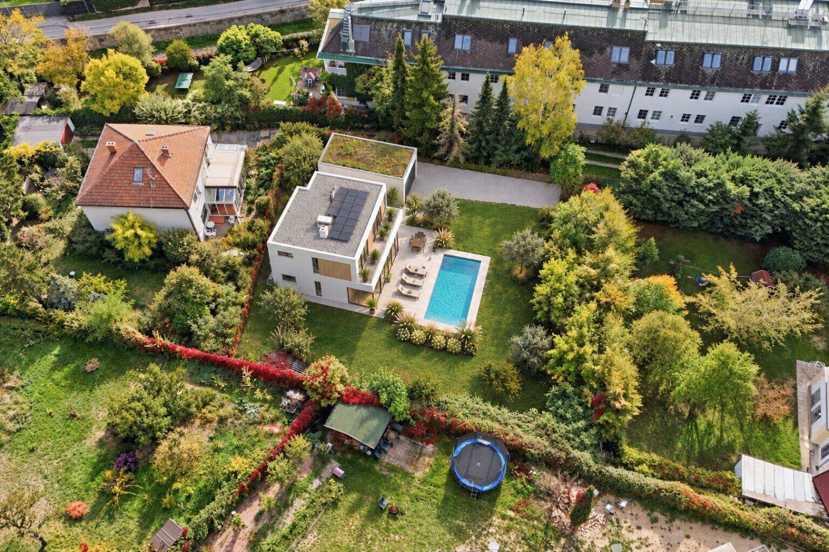Vogelperspektive einer modernen Villa mit Pool und Gründach, eingebettet in eine grüne Umgebung.