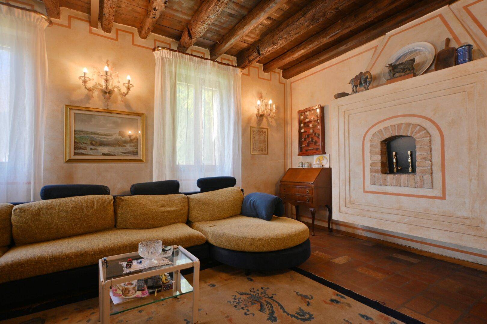 Gemütliches Wohnzimmer mit Ecksofa, Holzbalkendecke und einem traditionellen Kamin.