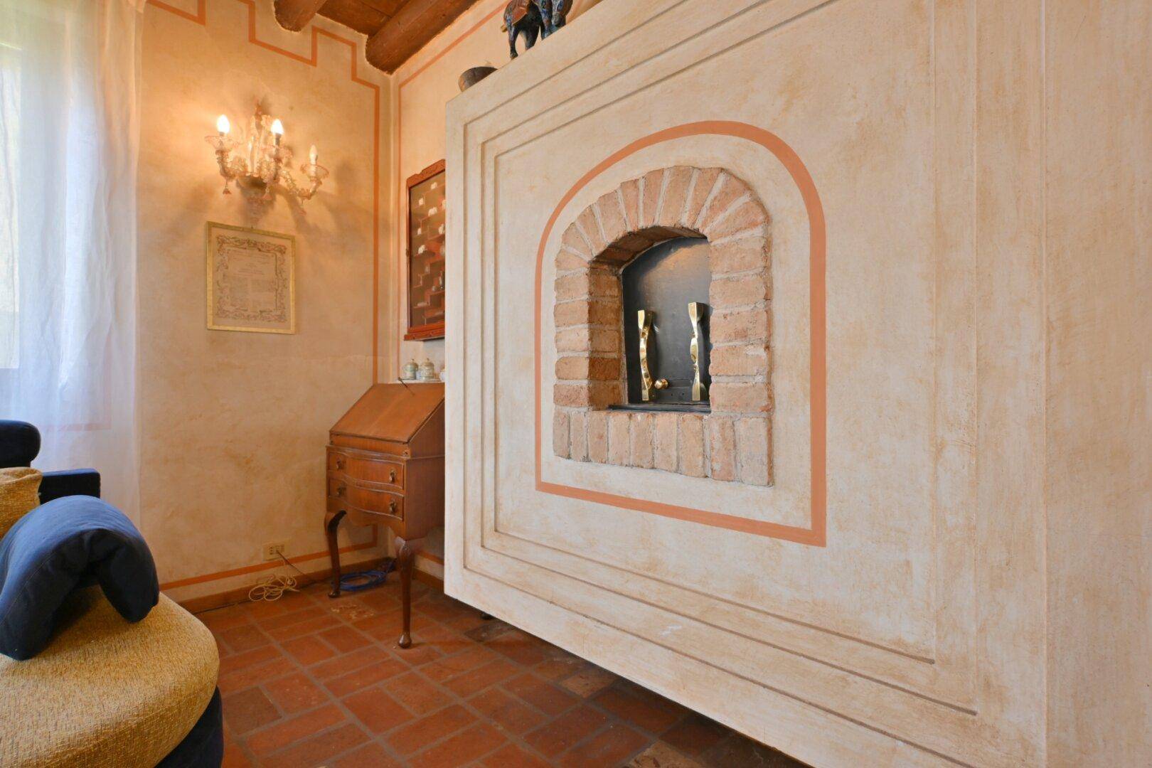 Detailansicht eines traditionellen Kamins mit Ziegelakzenten und Terrakottaboden im Wohnzimmer.