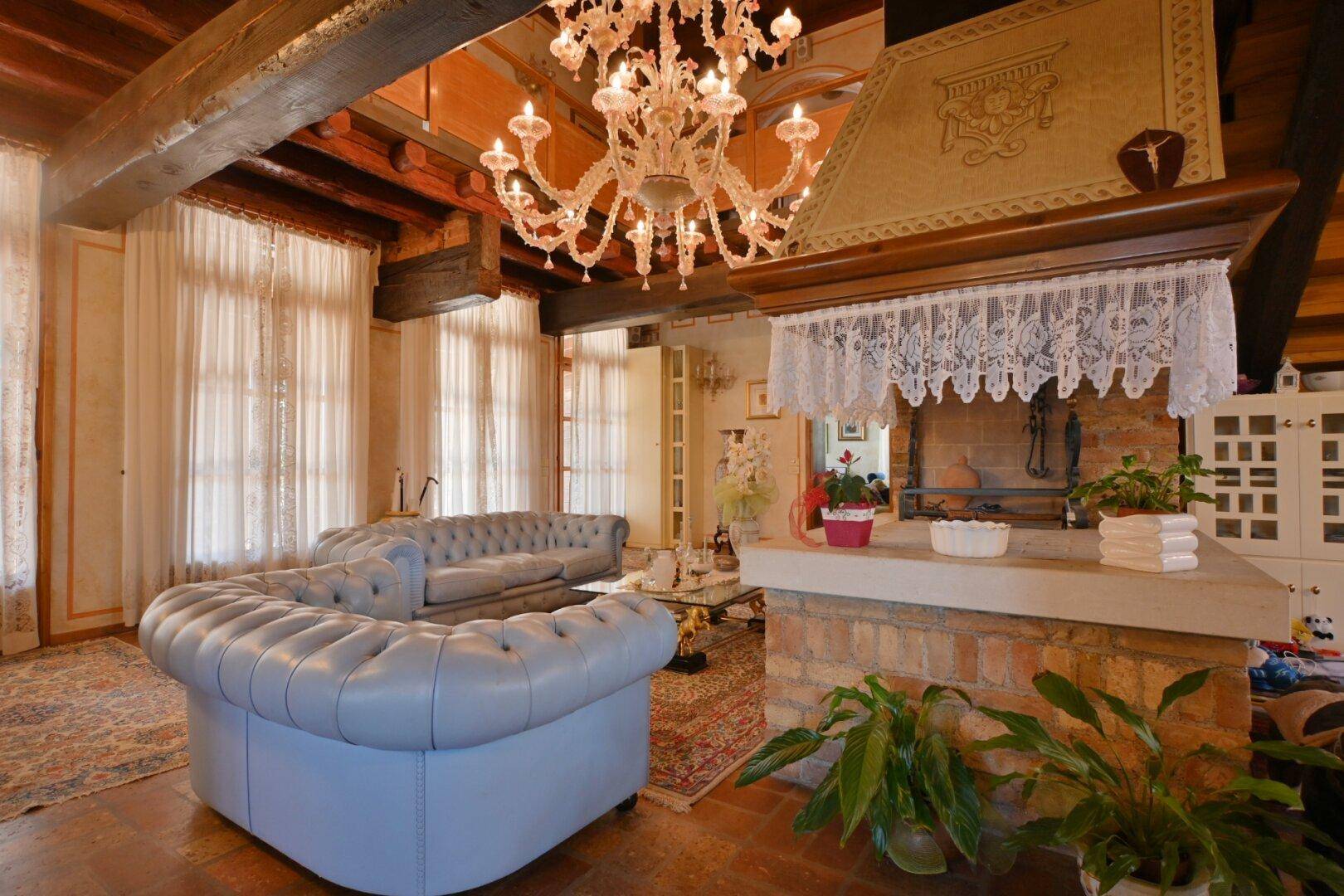 Geräumiges Wohnzimmer mit Chesterfield-Sofa, Holzbalkendecke und einem großen Kamin.
