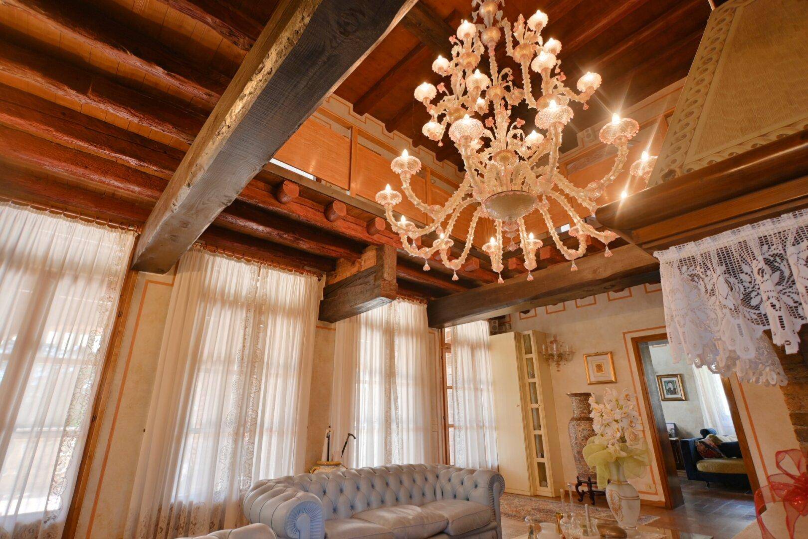 Prunkvolles Wohnzimmer mit Kronleuchter, Holzbalkendecke und hohen Fenstern für viel Licht.