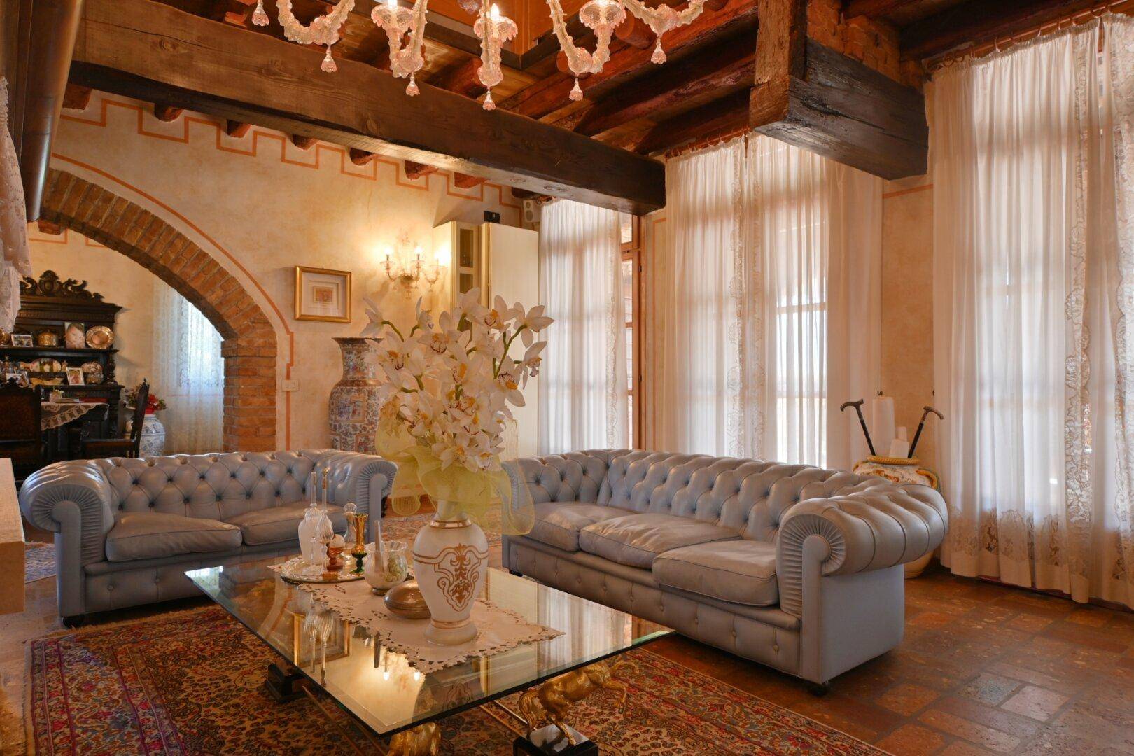 Elegantes Wohnzimmer mit Chesterfield-Sofas, Holzbalkendecke und großen Fenstern.
