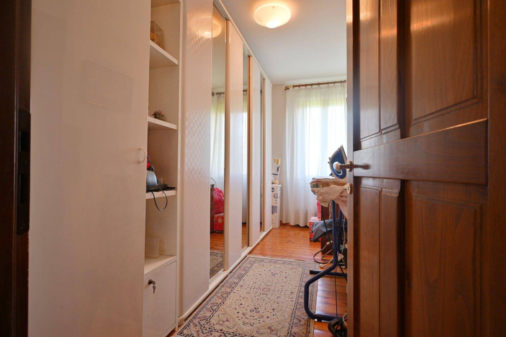 Langer Flur mit Spiegelschränken, Holzfußboden und Fenster mit Vorhängen.