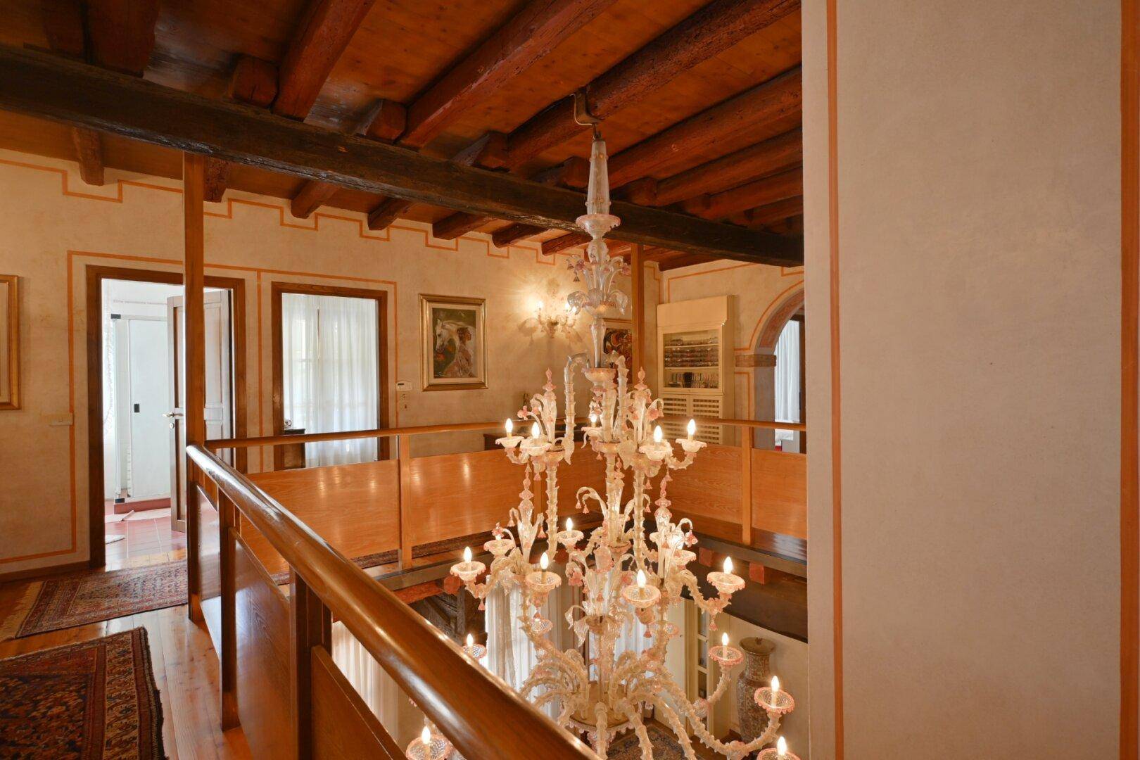 Elegantes Treppenhaus mit großem Kronleuchter, Holzbalkendecke und Galerieblick.