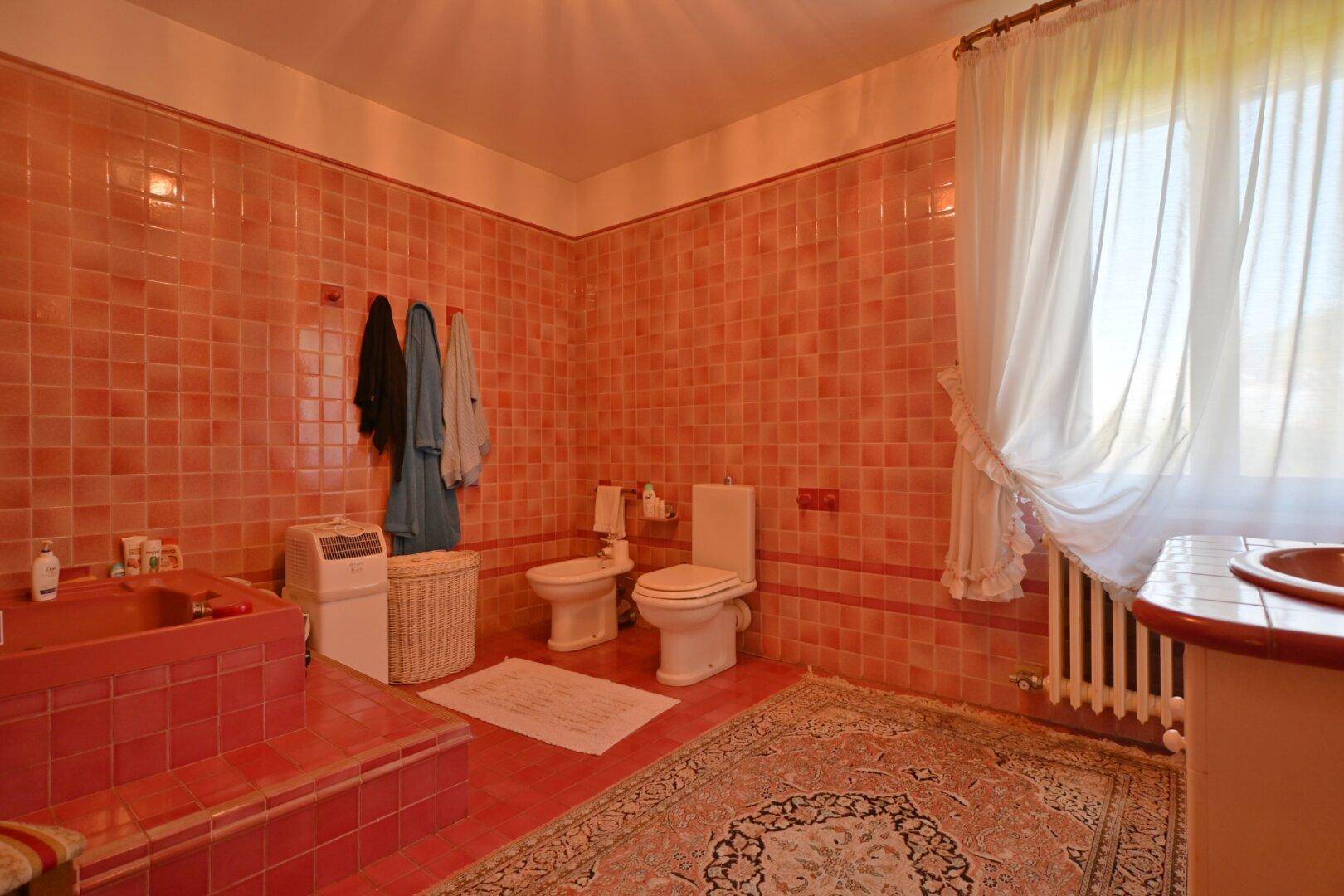 Geräumiges Badezimmer mit rosa Fliesen, Badewanne und Fenster mit Heizkörper.