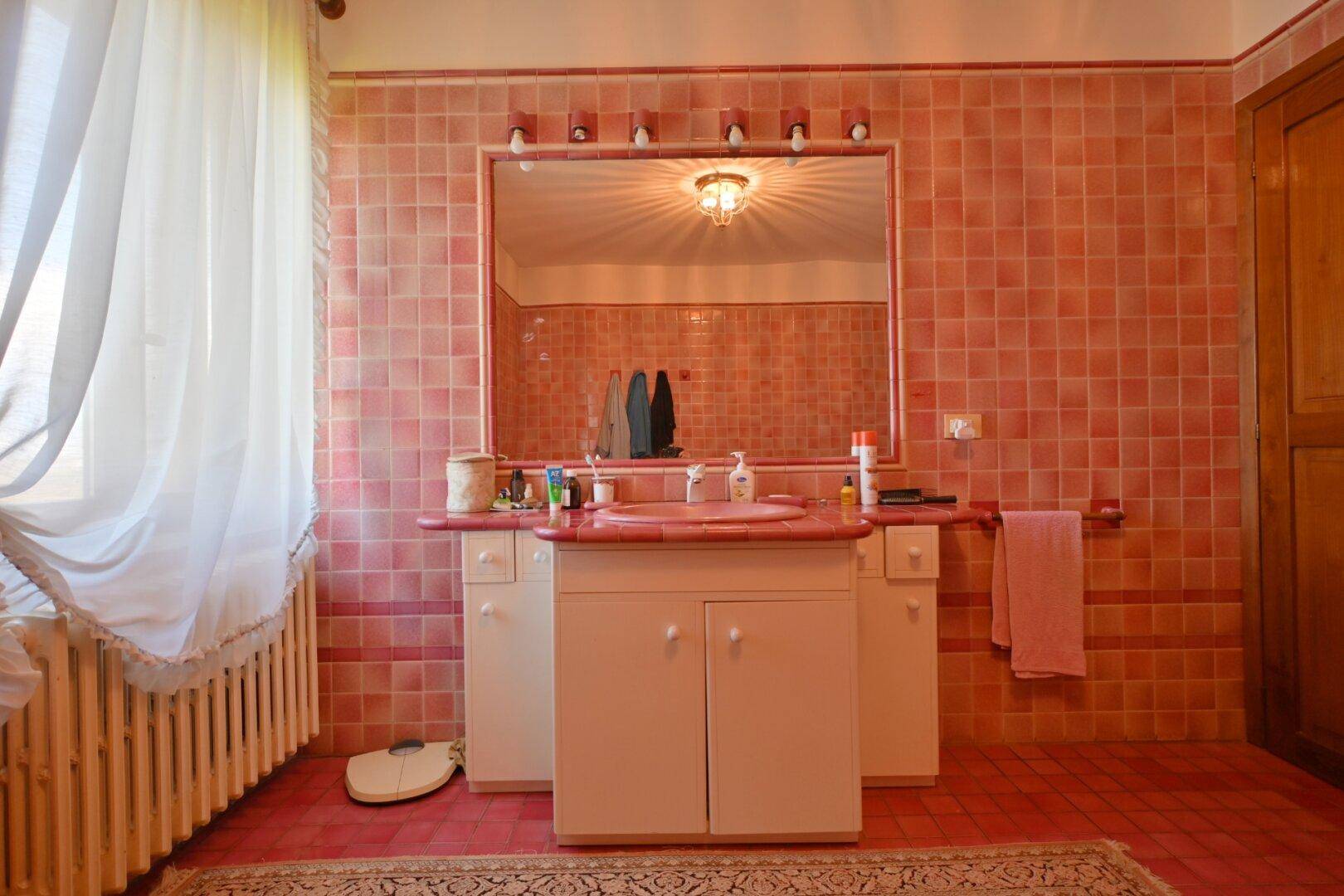 Badezimmer mit rosa Fliesen, Einzelwaschbecken und großem Spiegel über dem Waschtisch.