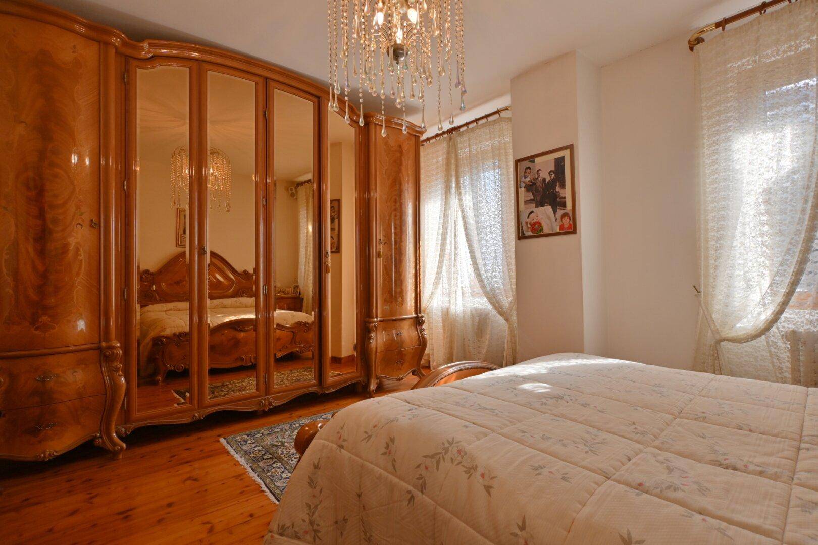 Schlafzimmer mit großem Holzschrank, Doppelbett und Kronleuchter.