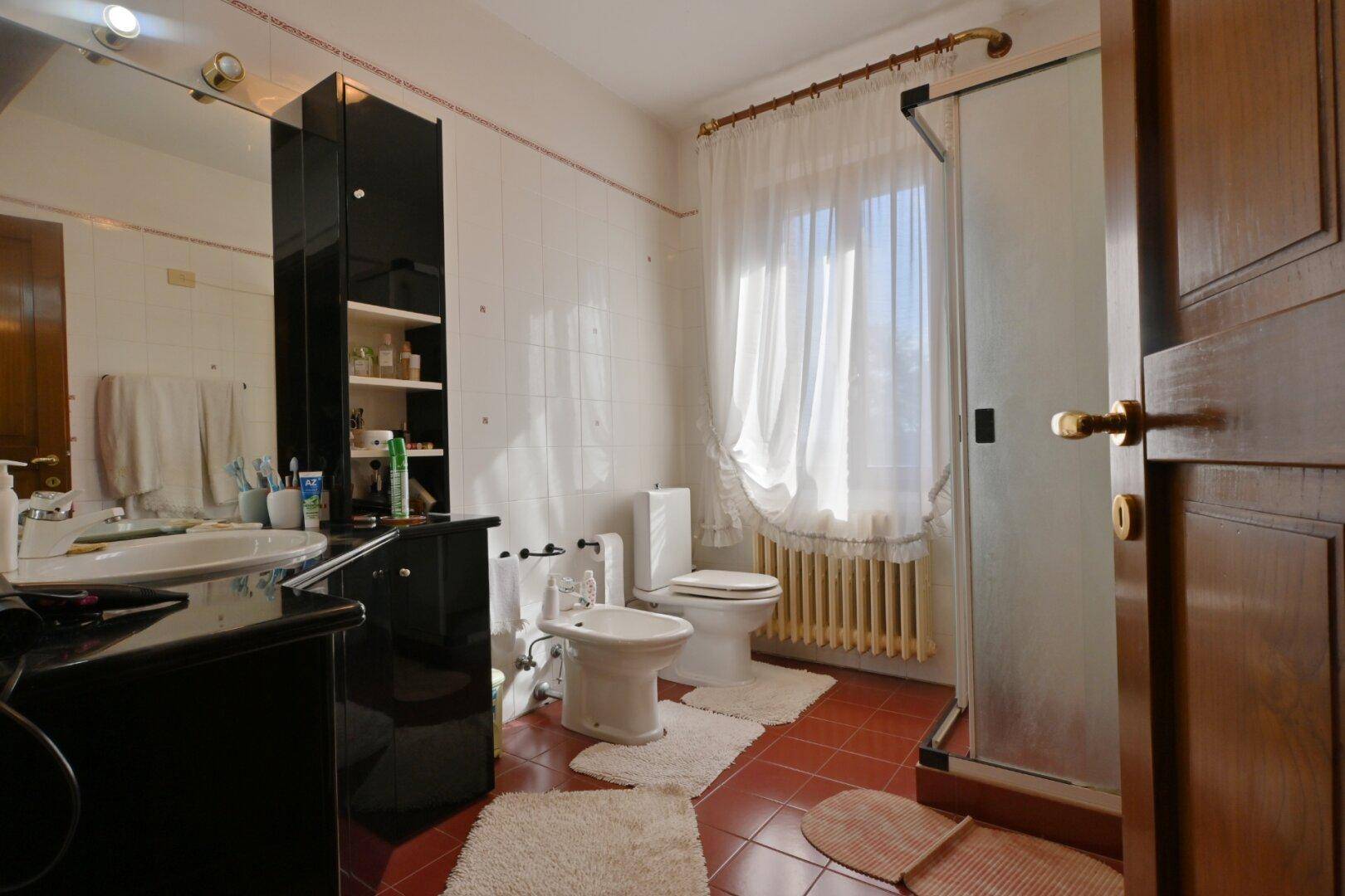Helles Badezimmer mit Duschkabine, Bidet und Fenster mit Heizkörper.