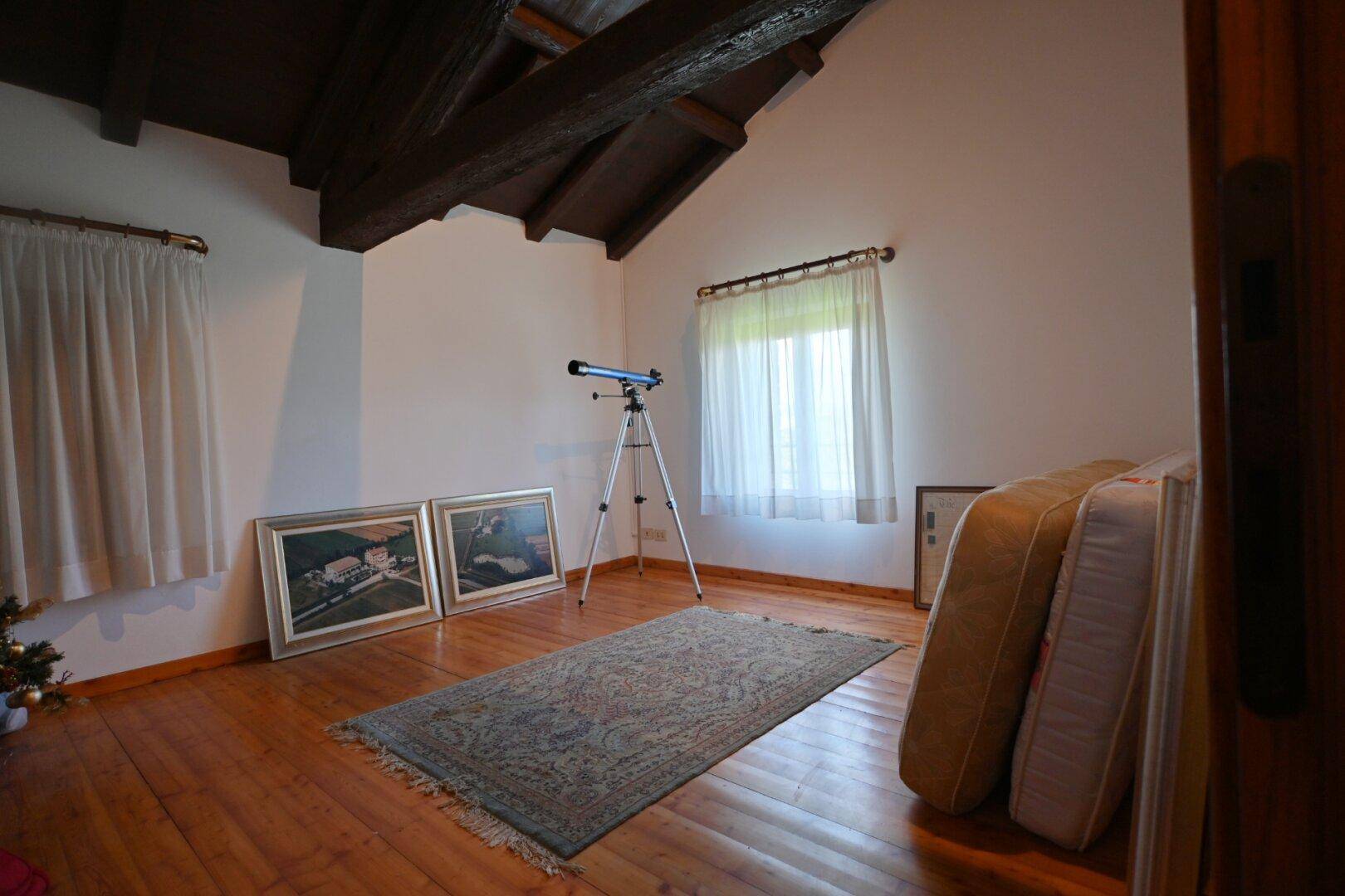 Dachzimmer mit Holzboden, schrägen Decken und Fenster mit Vorhängen.