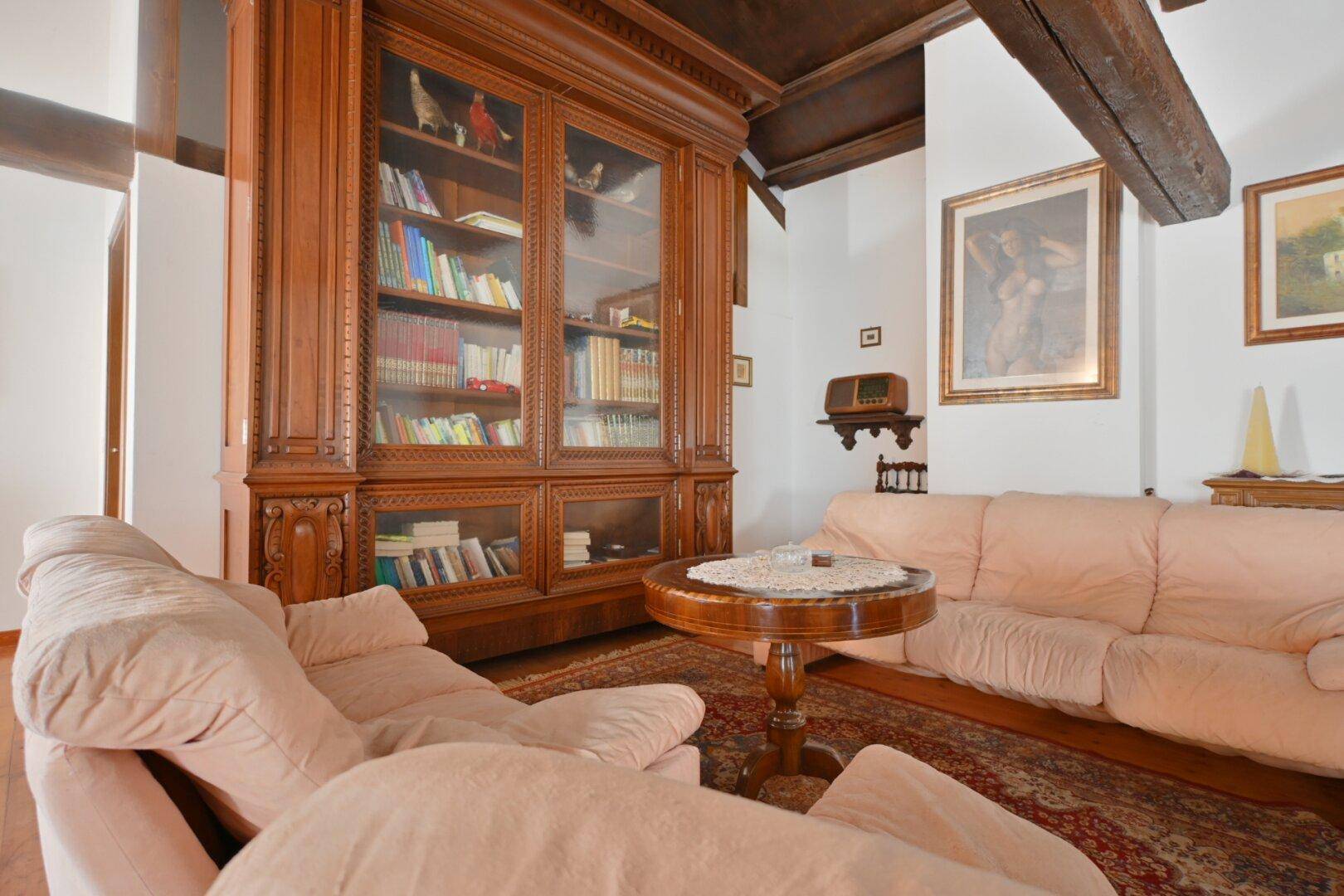 Gemütliches Wohnzimmer mit Holzbalkendecke, großem Bücherschrank und bequemen Sofas.