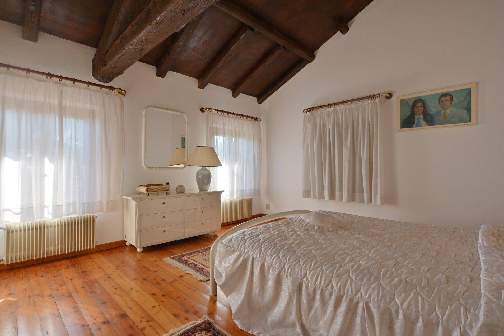 Helles Schlafzimmer mit Holzboden, Doppelbett und Kommode unter dem Fenster.