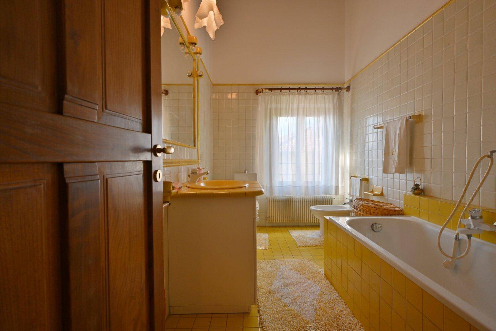 Badezimmer mit gelben Fliesen, Badewanne und Fenster mit Heizkörper.