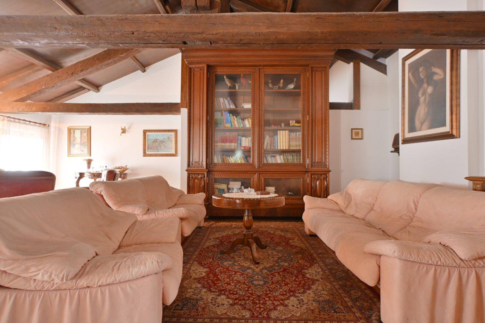Gemütliches Wohnzimmer mit Holzbalkendecke, traditionellem Teppich und großem Bücherregal.
