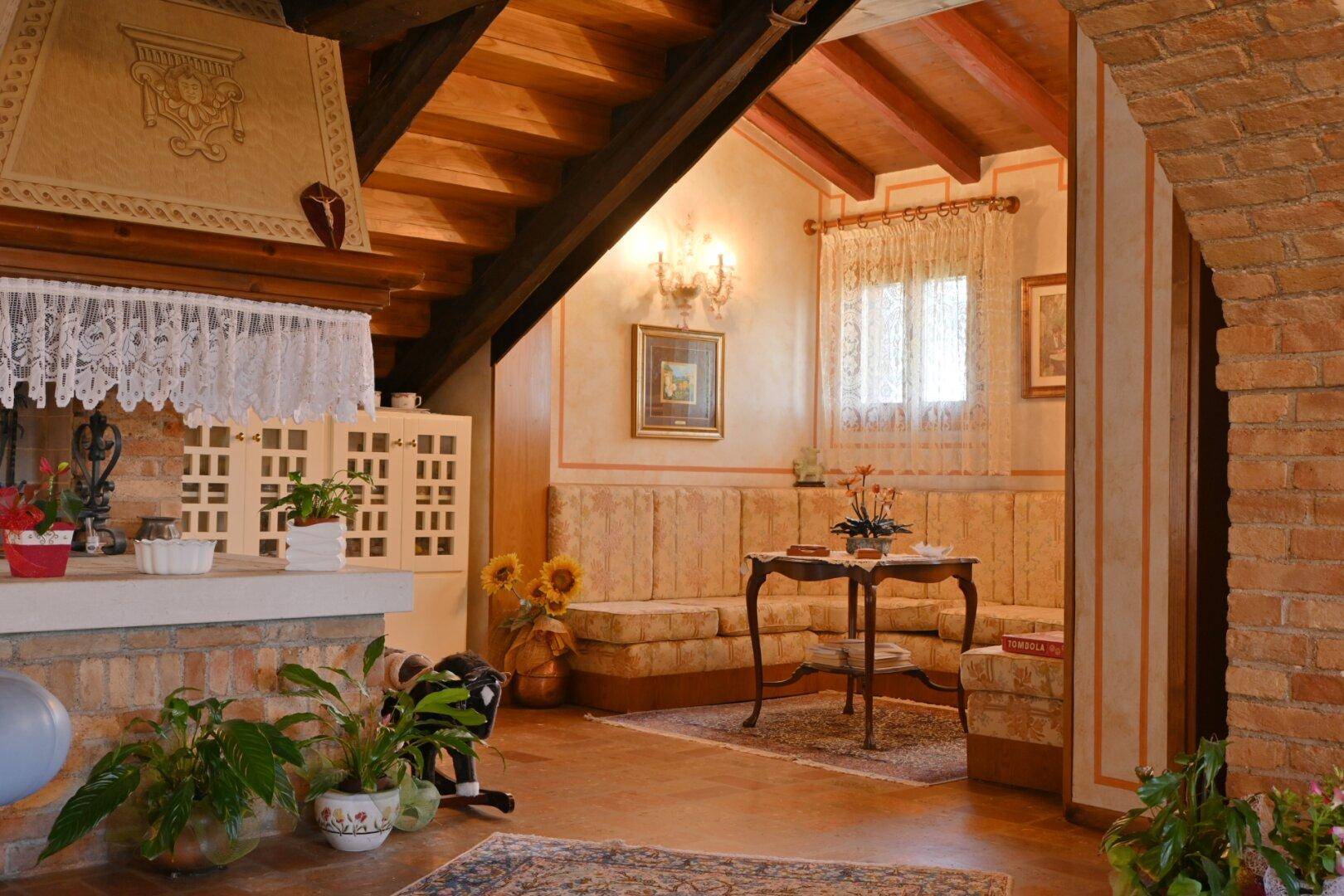 Rustikaler Sitzbereich mit Holzbalkendecke, Terrakottaboden und einem traditionellen Kamin.