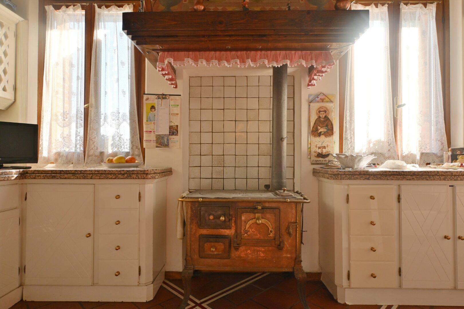 Rustikale Küche mit traditionellem Holzofen, gefliesten Arbeitsflächen und hellen Fenstern.
