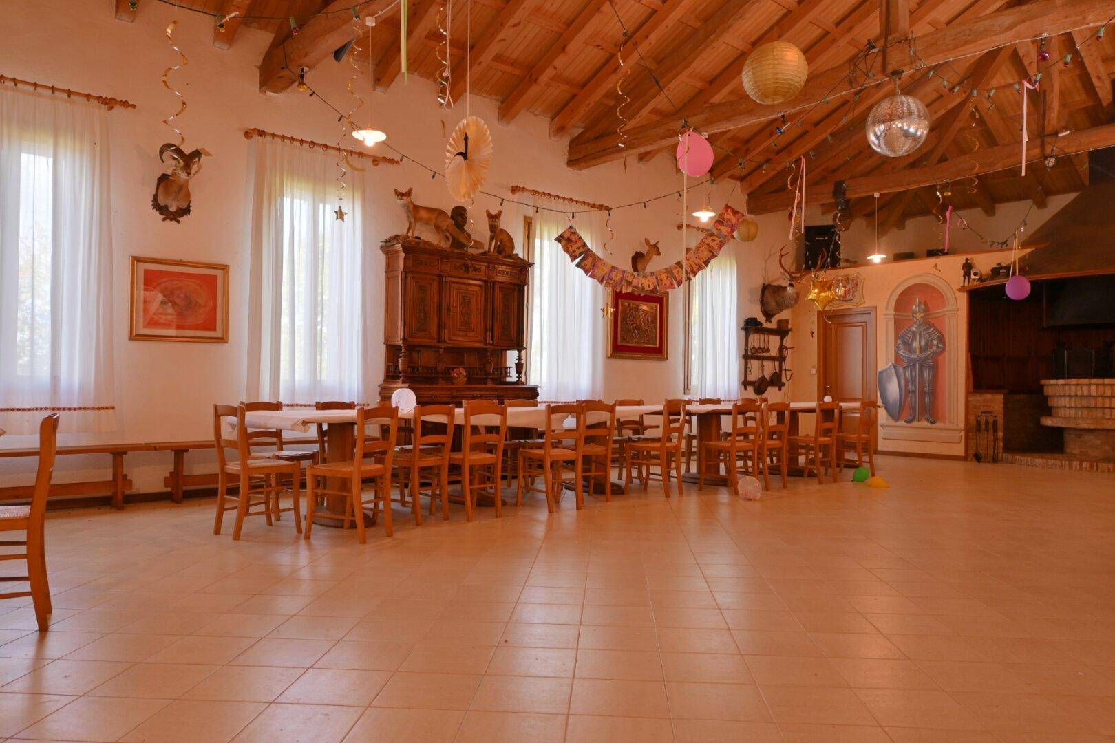 Großer Speisesaal mit Holzbalkendecke, vielen Tischen und festlicher Dekoration.