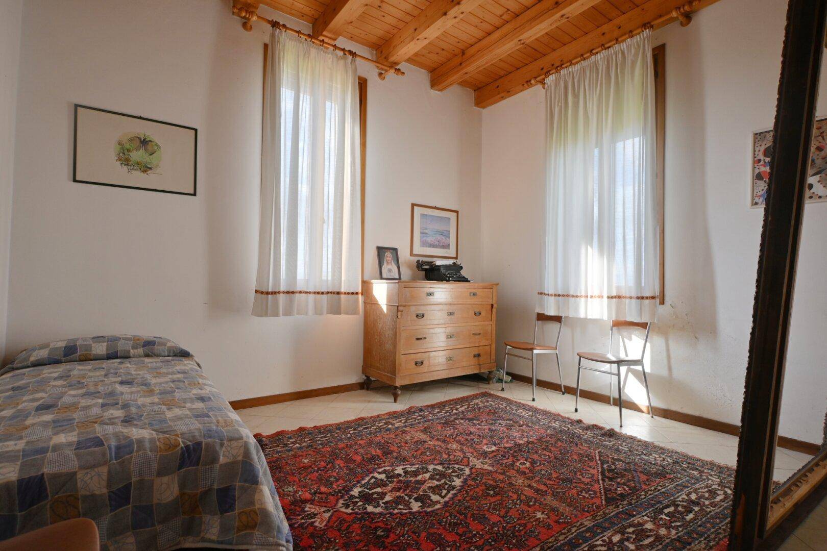 Helles Schlafzimmer mit Holzbalkendecke, Einzelbett und traditionellem Teppich.