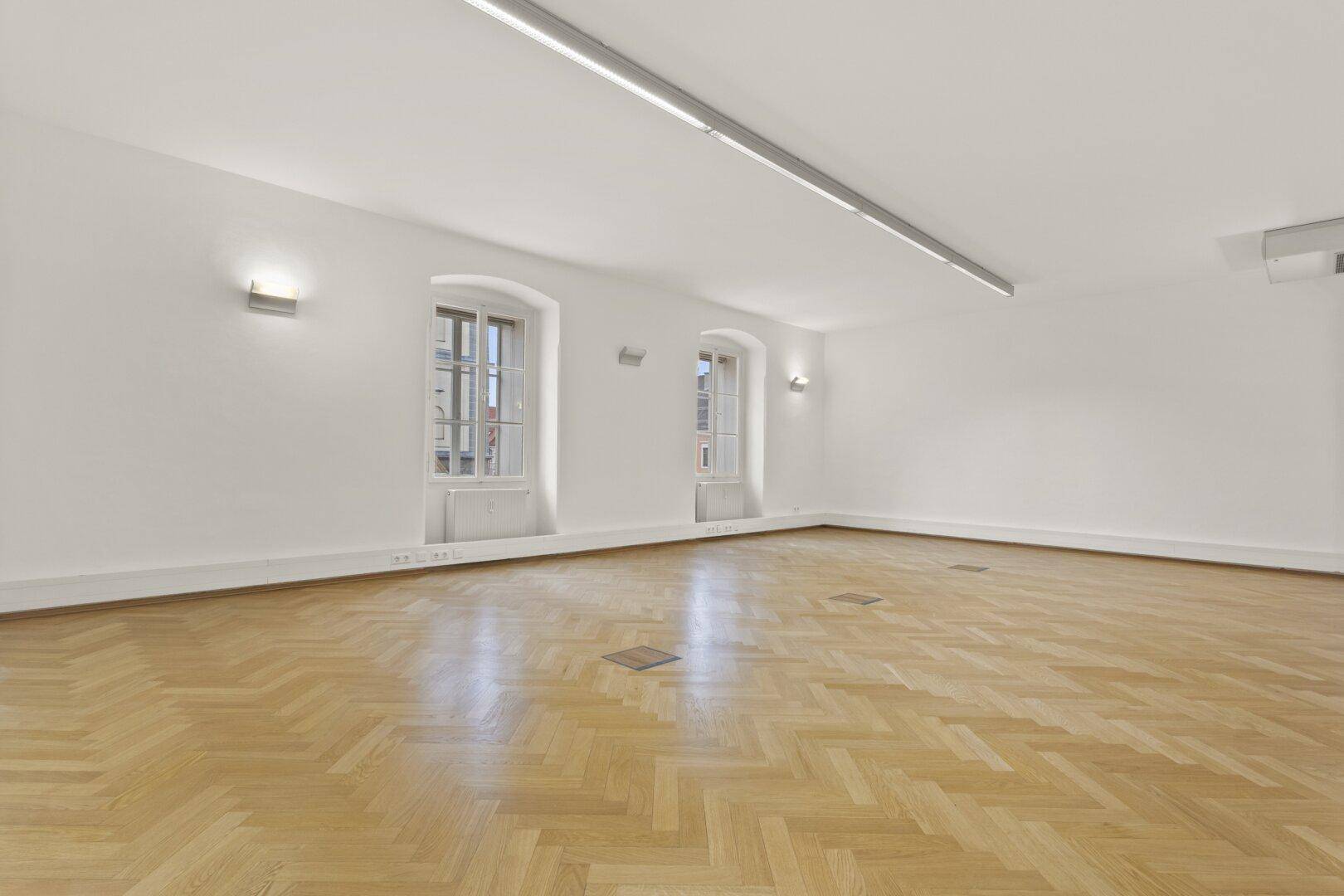 Heller, leerer Raum mit Fischgrätparkett und zwei hohen Bogenfenstern, ideal für Büronutzung.
