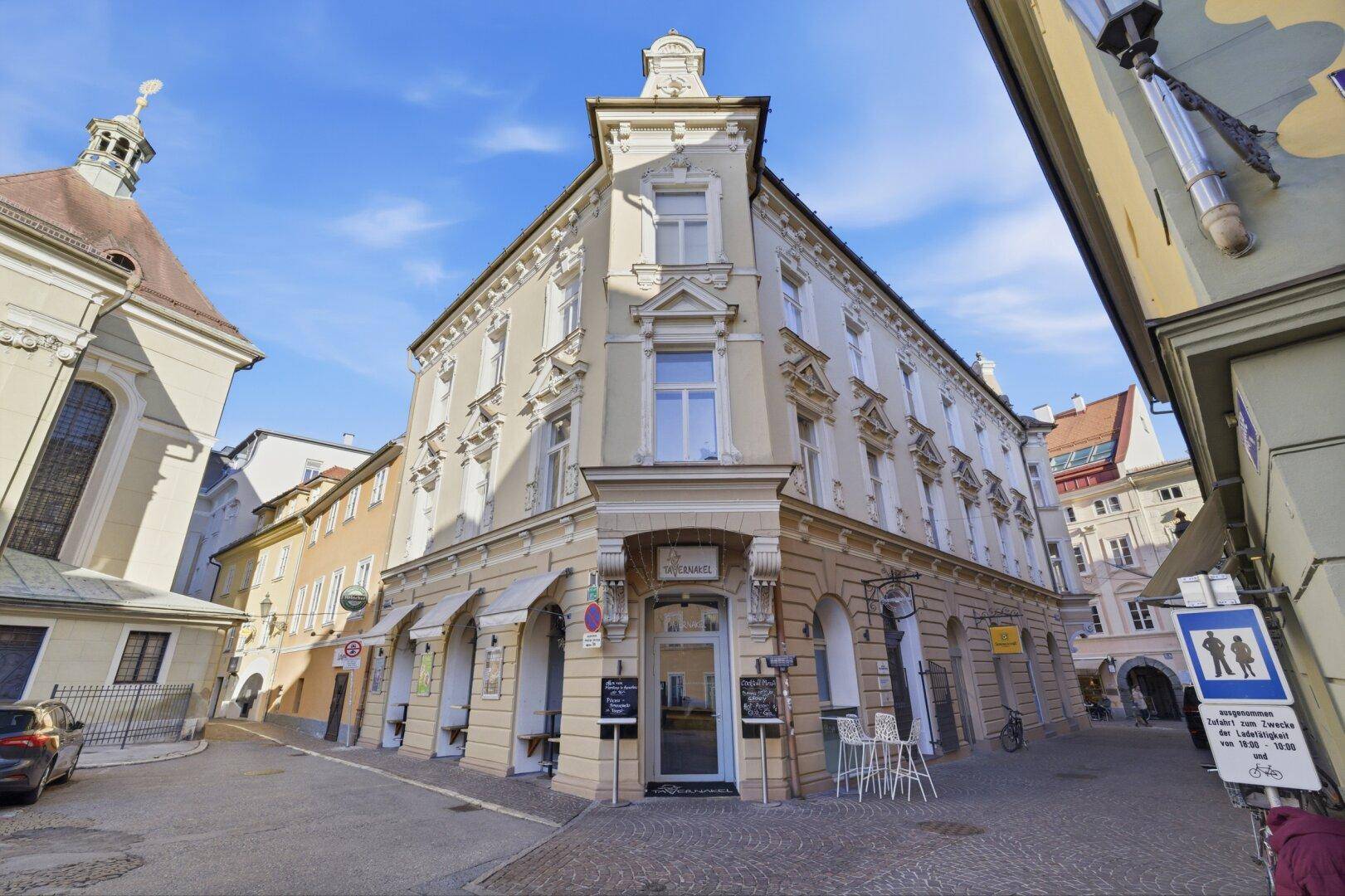 Historisches Eckgebäude mit klassischer Architektur und Geschäften im Erdgeschoss in einer belebten Straße.