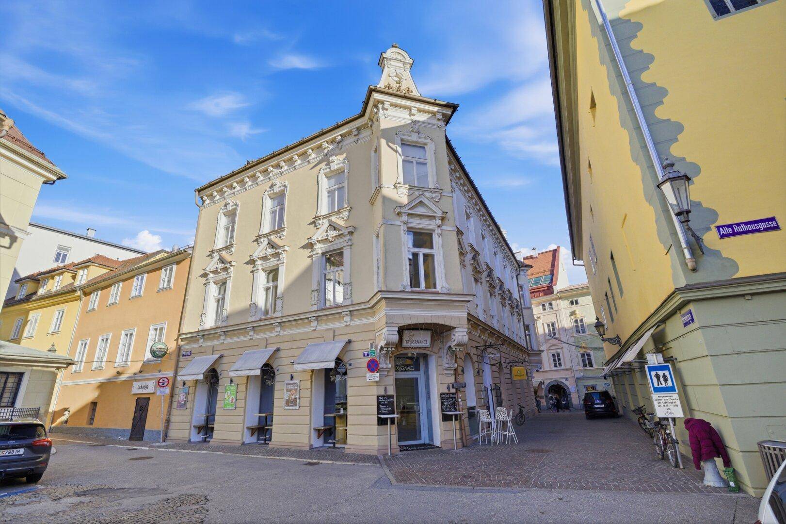Charmantes Eckhaus in einer belebten Straße mit traditioneller Architektur und Geschäften im Erdgeschoss.