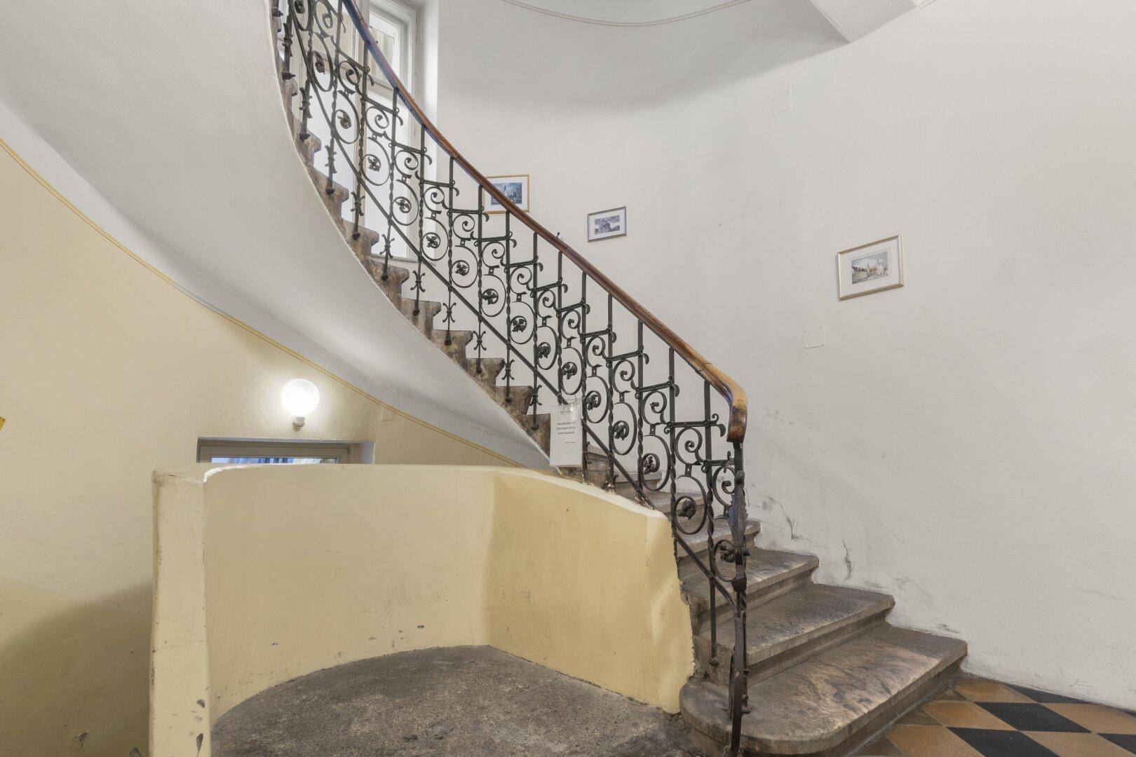 Elegantes Treppenhaus mit geschwungenem Geländer aus Schmiedeeisen, Marmorstufen und Fliesenboden.