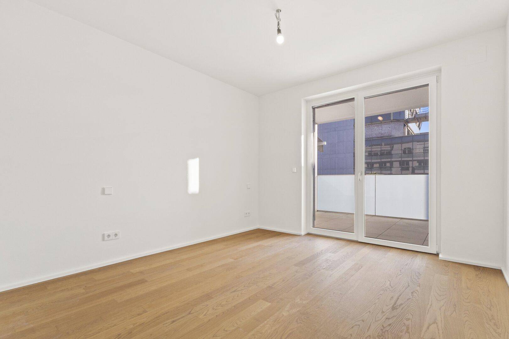 Helles Zimmer mit Parkettboden und großer Schiebetür, die auf einen Balkon führt.
