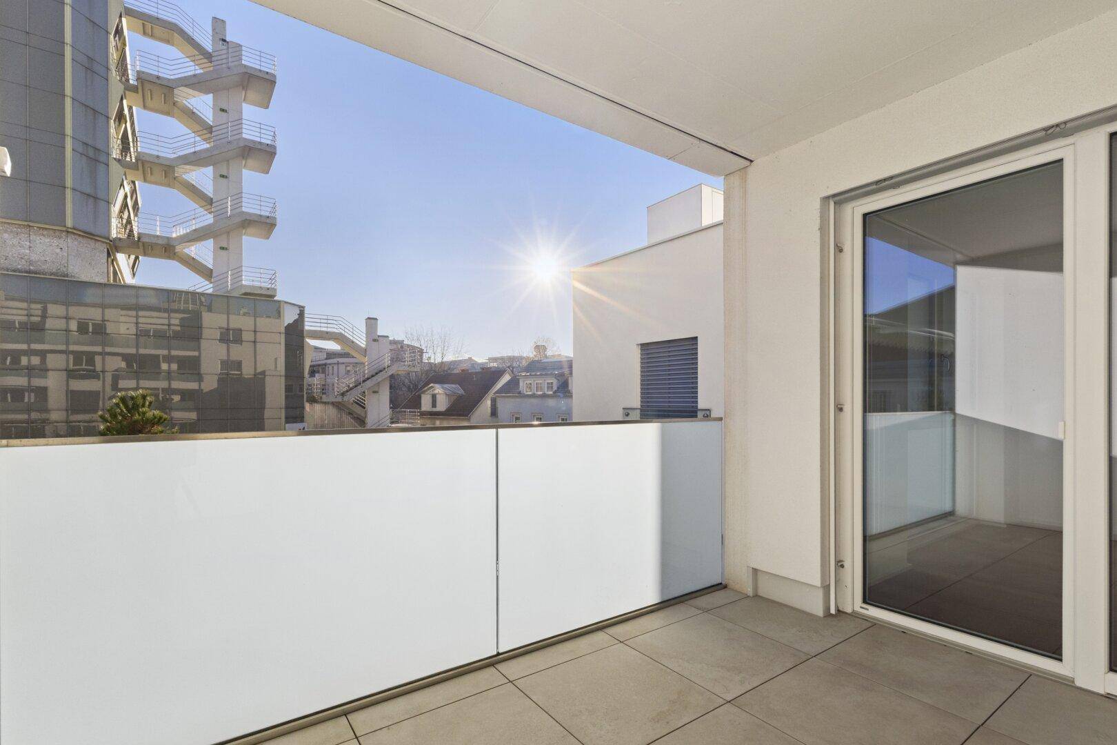 Sonniger Balkon mit Fliesenboden und moderner Glasbrüstung, bietet einen Blick auf die Umgebung.
