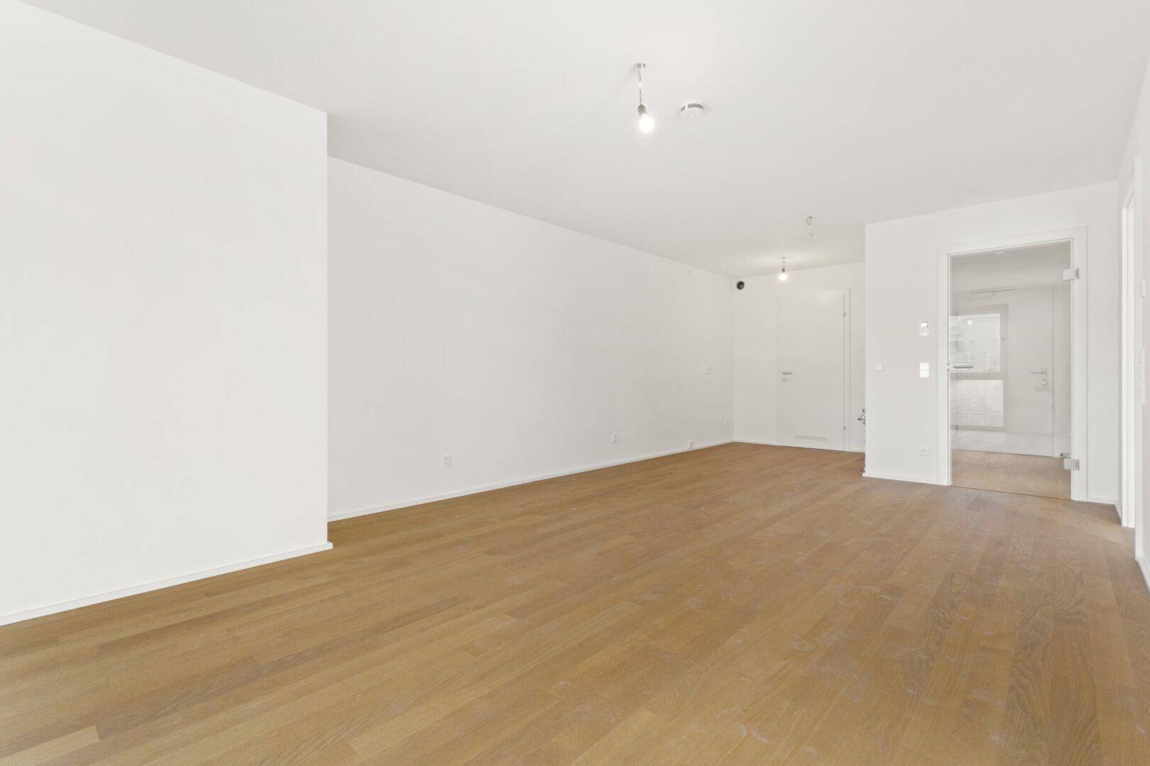 Geräumiges Wohnzimmer mit hellem Parkettboden und weiß gestrichenen Wänden, bereit zur Einrichtung.