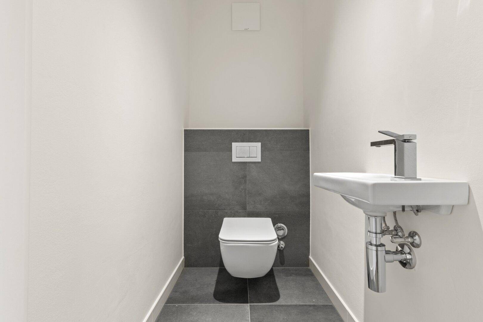 Kompaktes Gäste-WC mit wandhängender Toilette und kleinem Waschbecken.